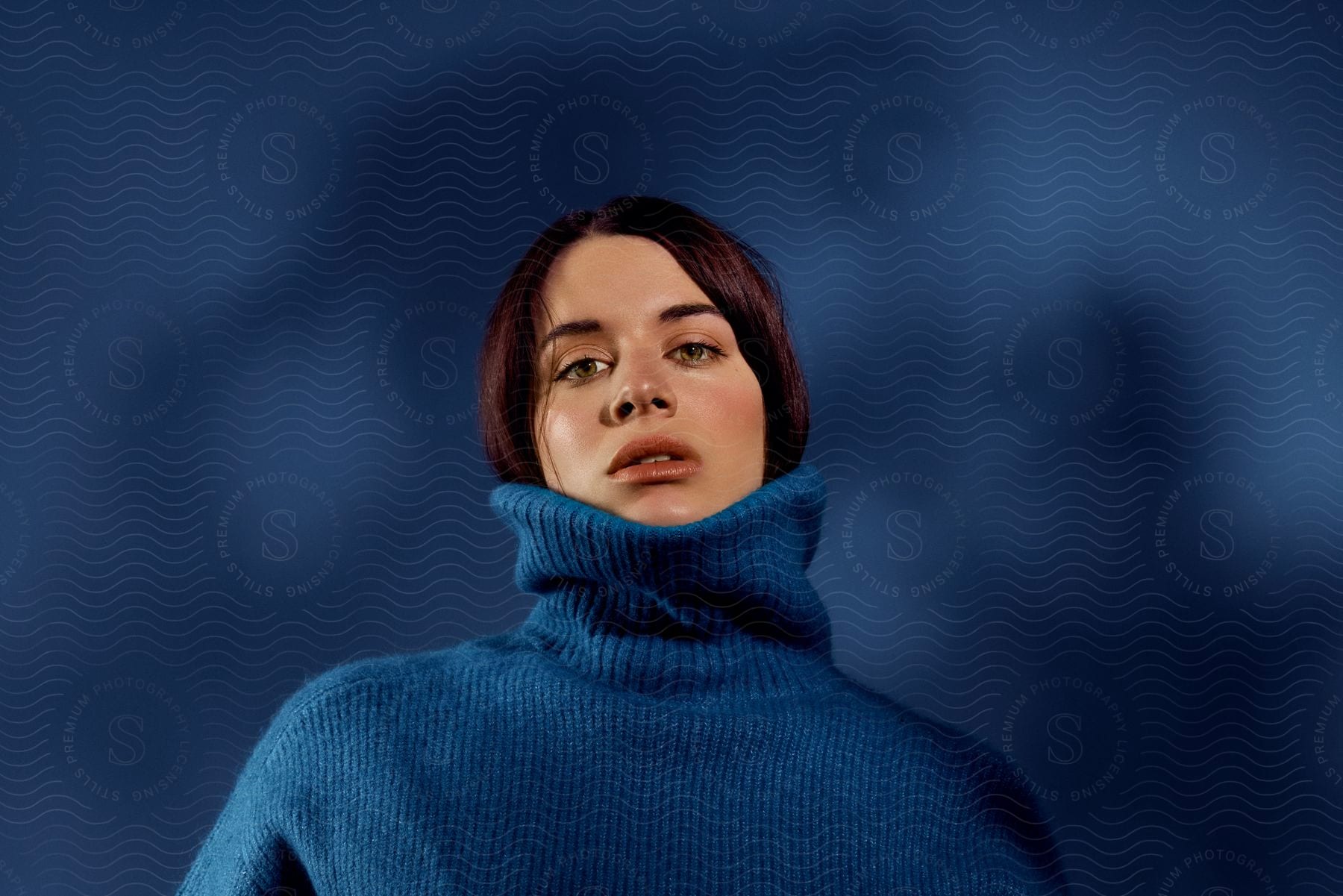 Woman in blue turtleneck sweater against a blue background.