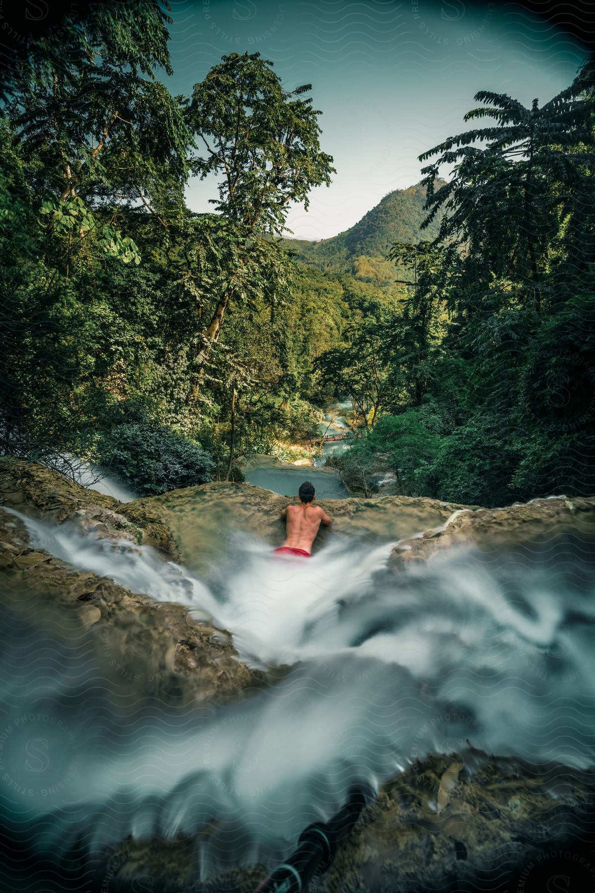 Man on his back and lying on a rock in the middle of a flowing river in the forest during the day