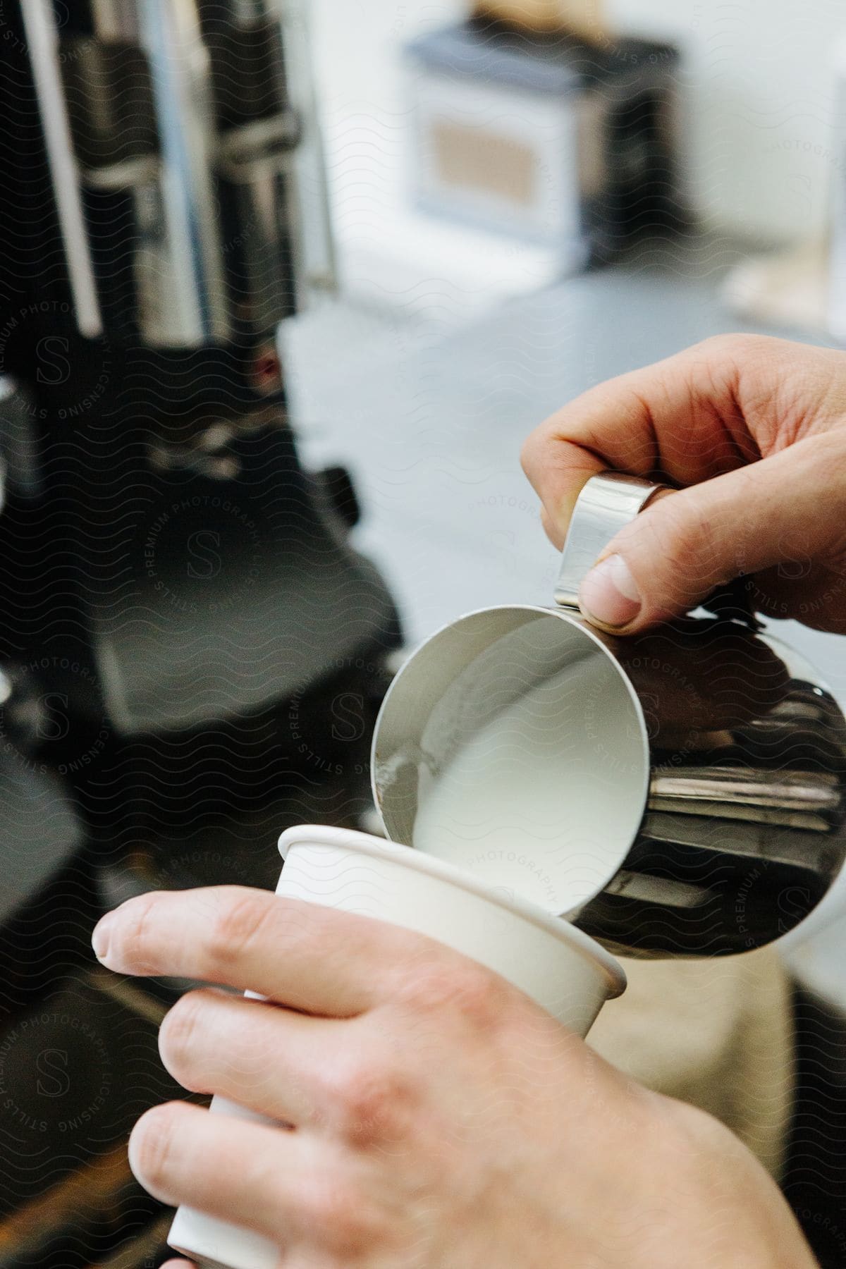 Hands of a person pouring a cup of milk into a disposable cup