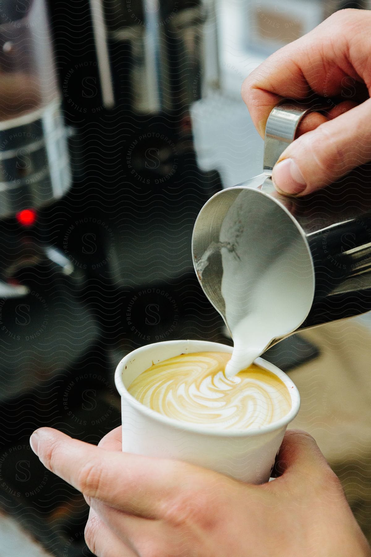 Human hands pouring milk from a mug into a cup of coffee and making a drawing on the surface