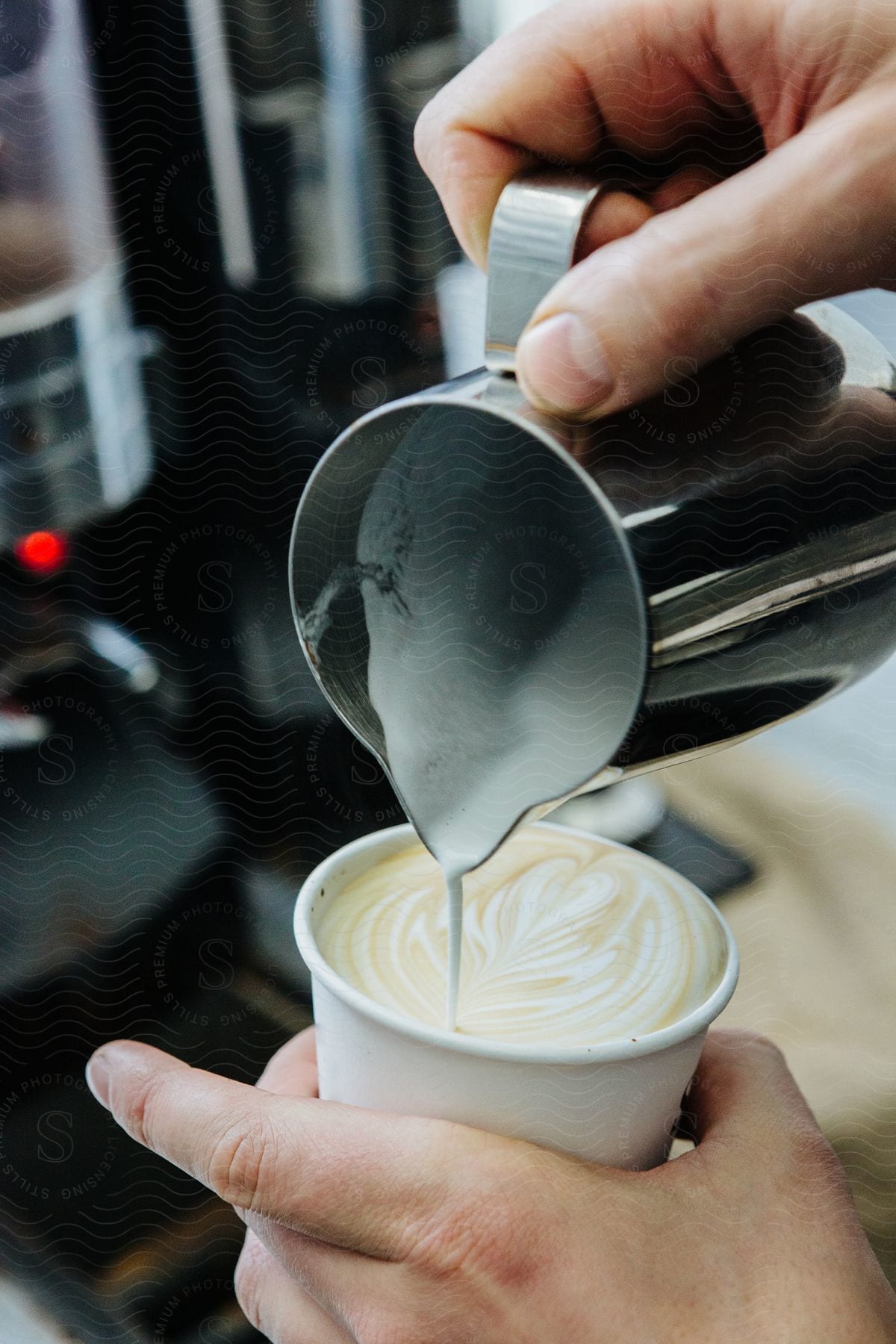 a person pouring milk from a silver pitcher held in their right hand, into a white mug in their left hand.