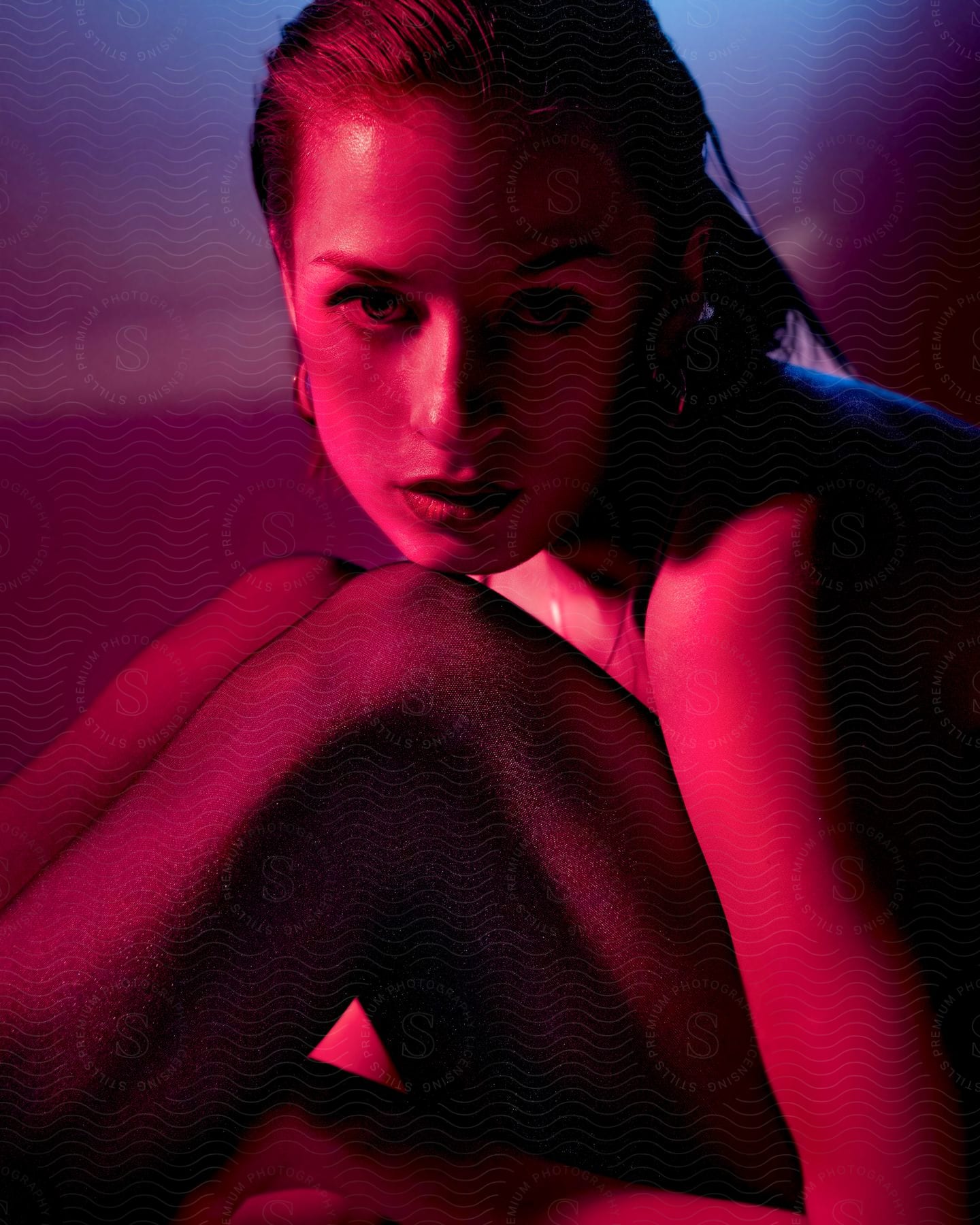 Female models posed chin on knee under red studio lighting
