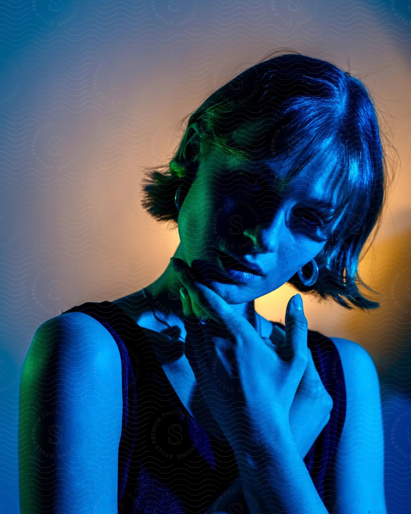 A woman is holding her chin with her left hand and looking straight ahead while her skin is illuminated by a blue light