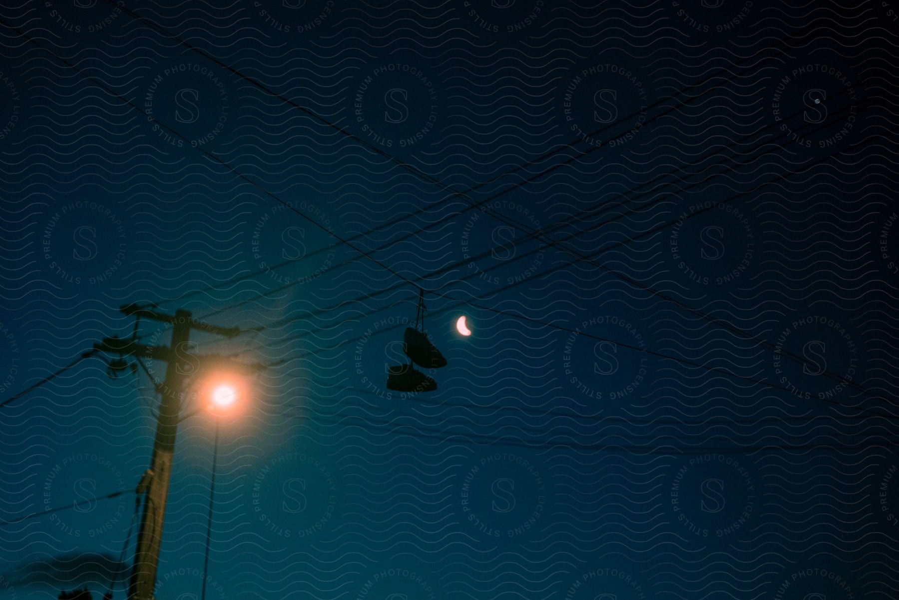 An electrical pole with lines and a crescent moon in the background in the night sky.