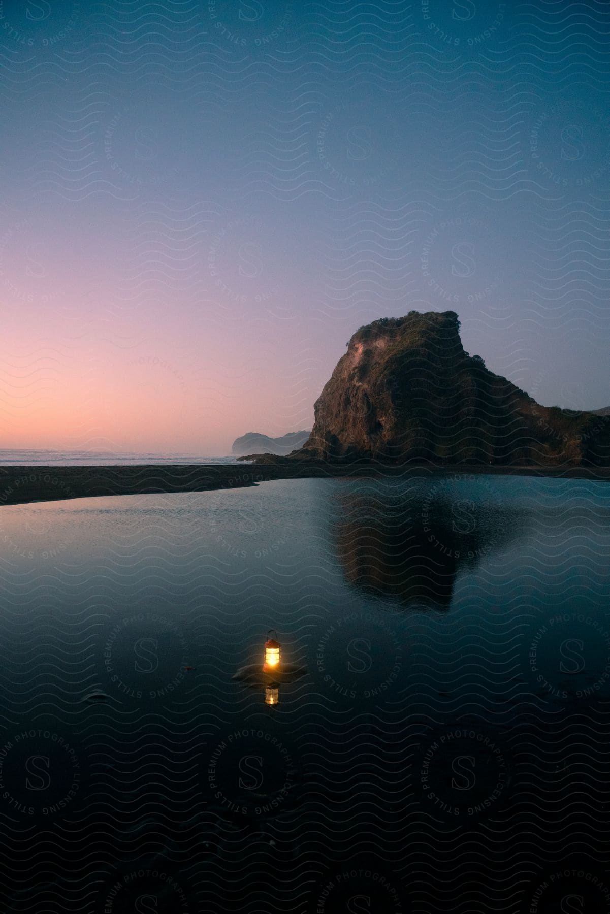 A lantern on the water below a mountainous outcropping.