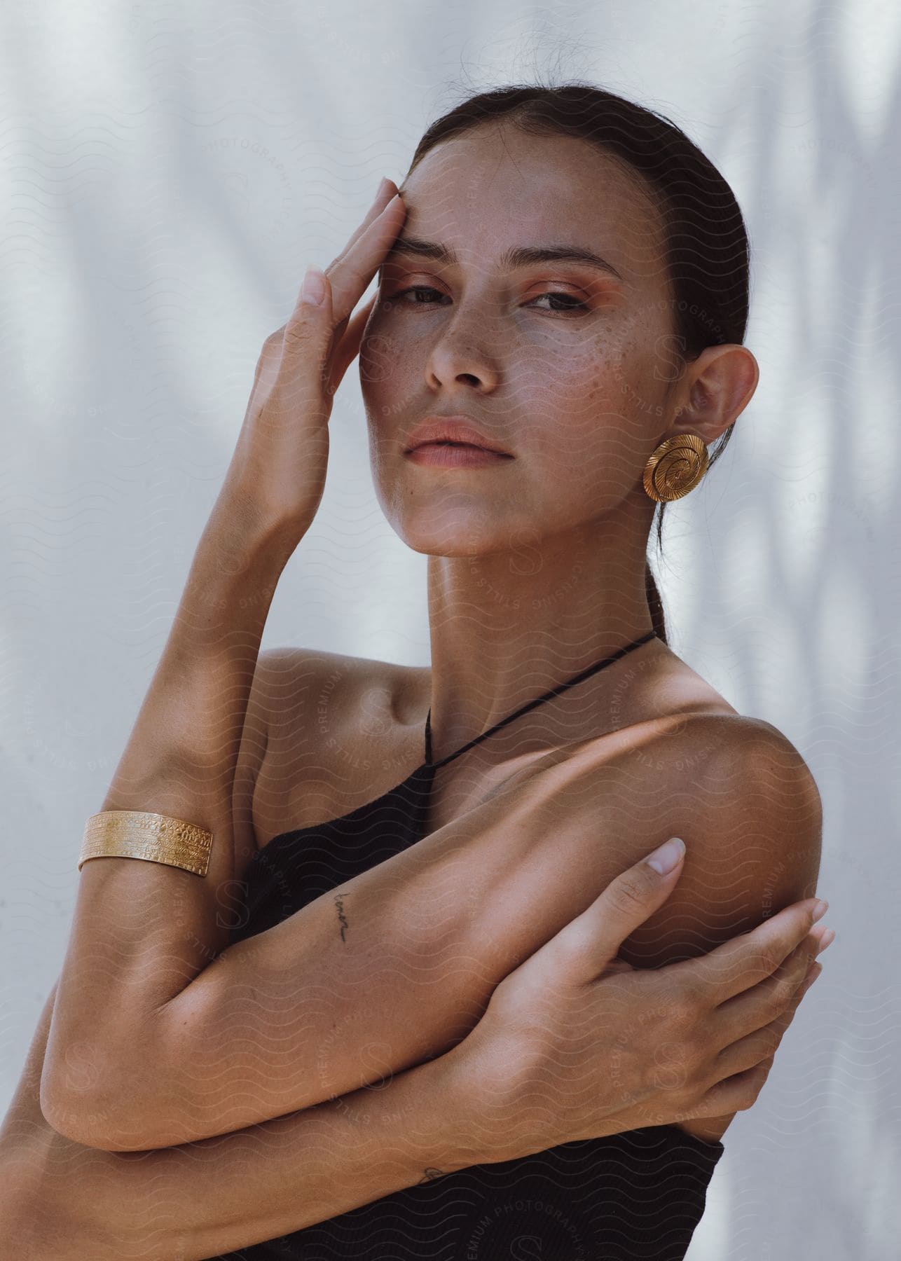 A dark haired woman with freckles hugging herself.