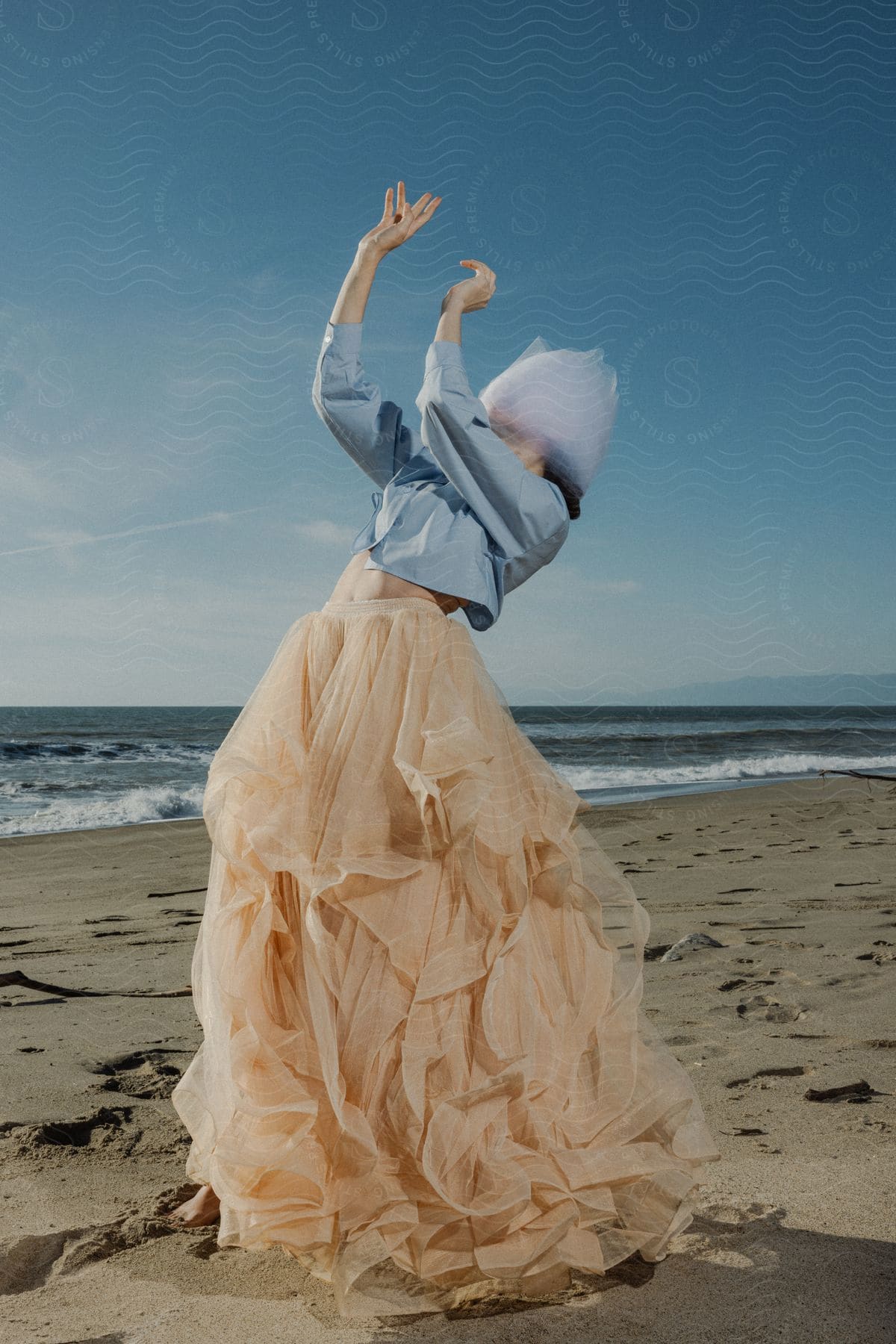 A woman wearing a skirt is dancing on the beach with a cloth wrapped around her head