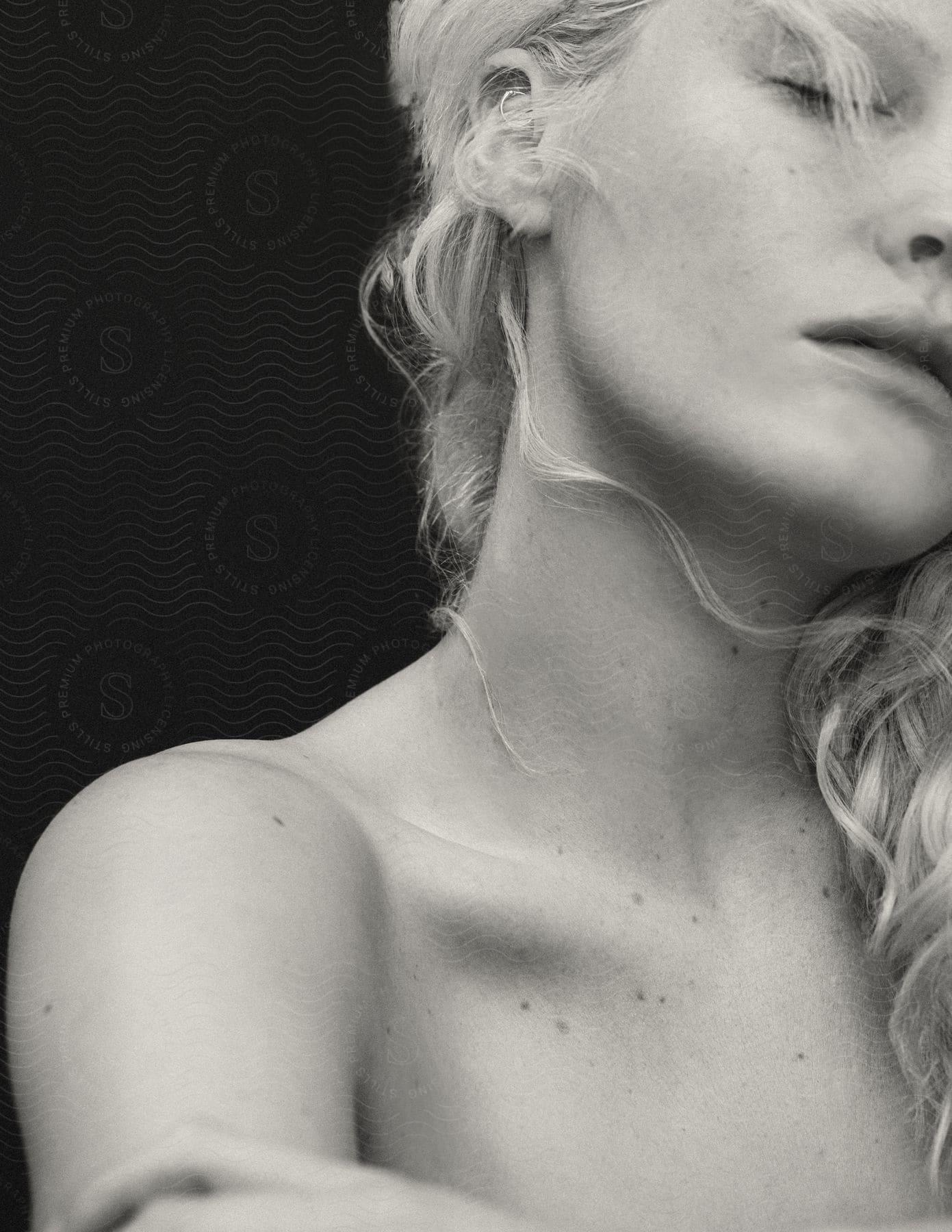 Close-up of a woman with blonde hair and closed eyes, showing her shoulder and neck, black background.Close-up of a woman with blonde hair and closed eyes, showing her shoulder and neck, black background.