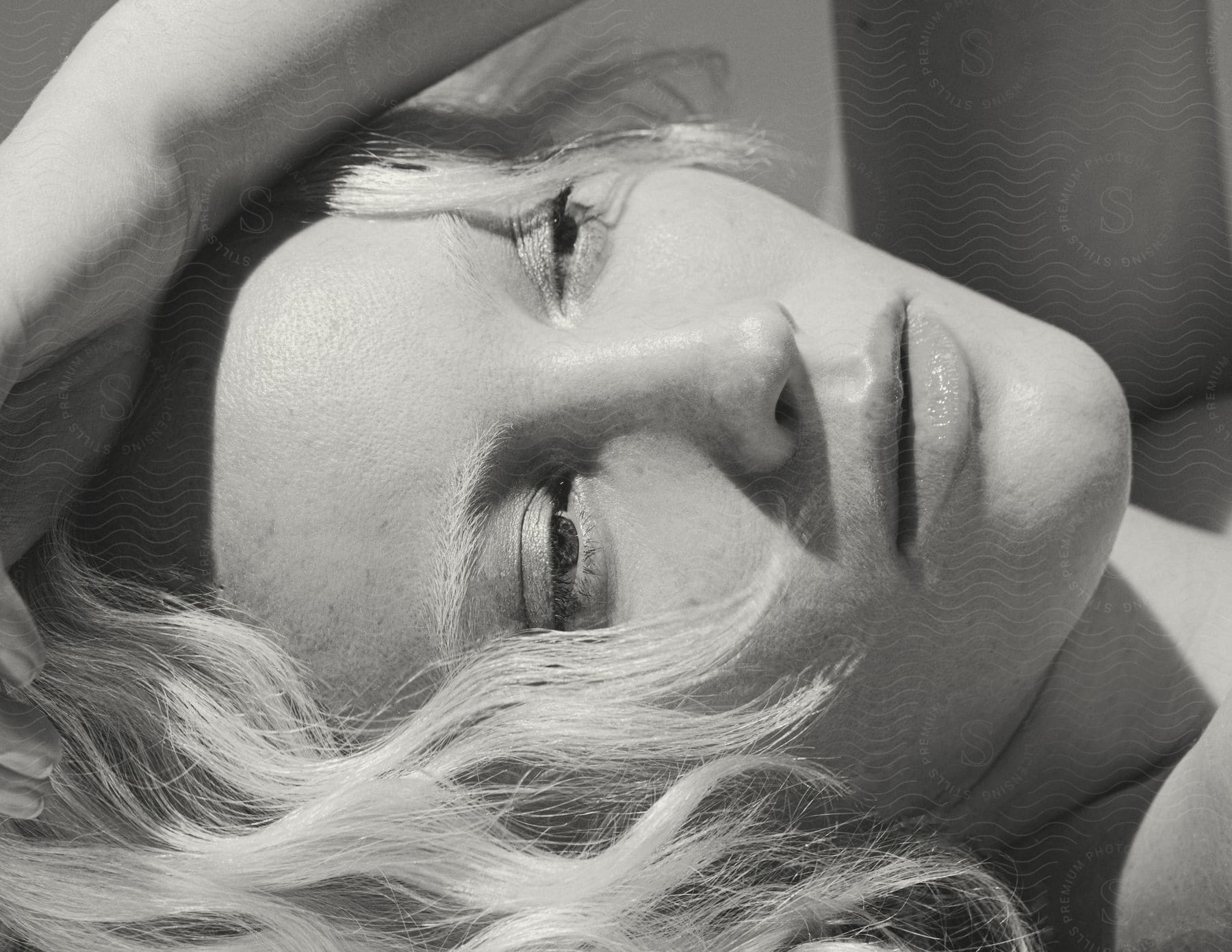 The Sun Shines On The Face Of A Young Blonde Woman Lying Outside With Her Arm Over Her Head