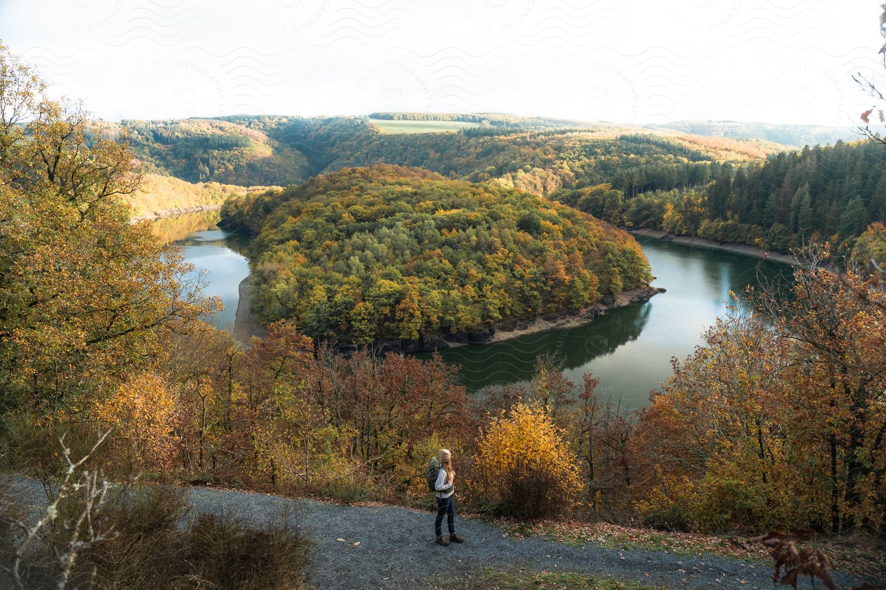 Woman hiking on a gravel road next to a lake with a forested island in the center.