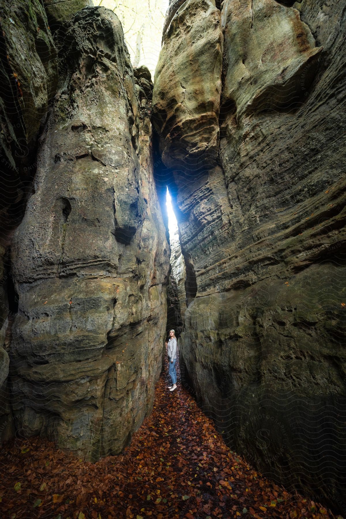 Woman standing in a narrow, rocky gorge with a sliver of sky visible above and autumn leaves on the ground.