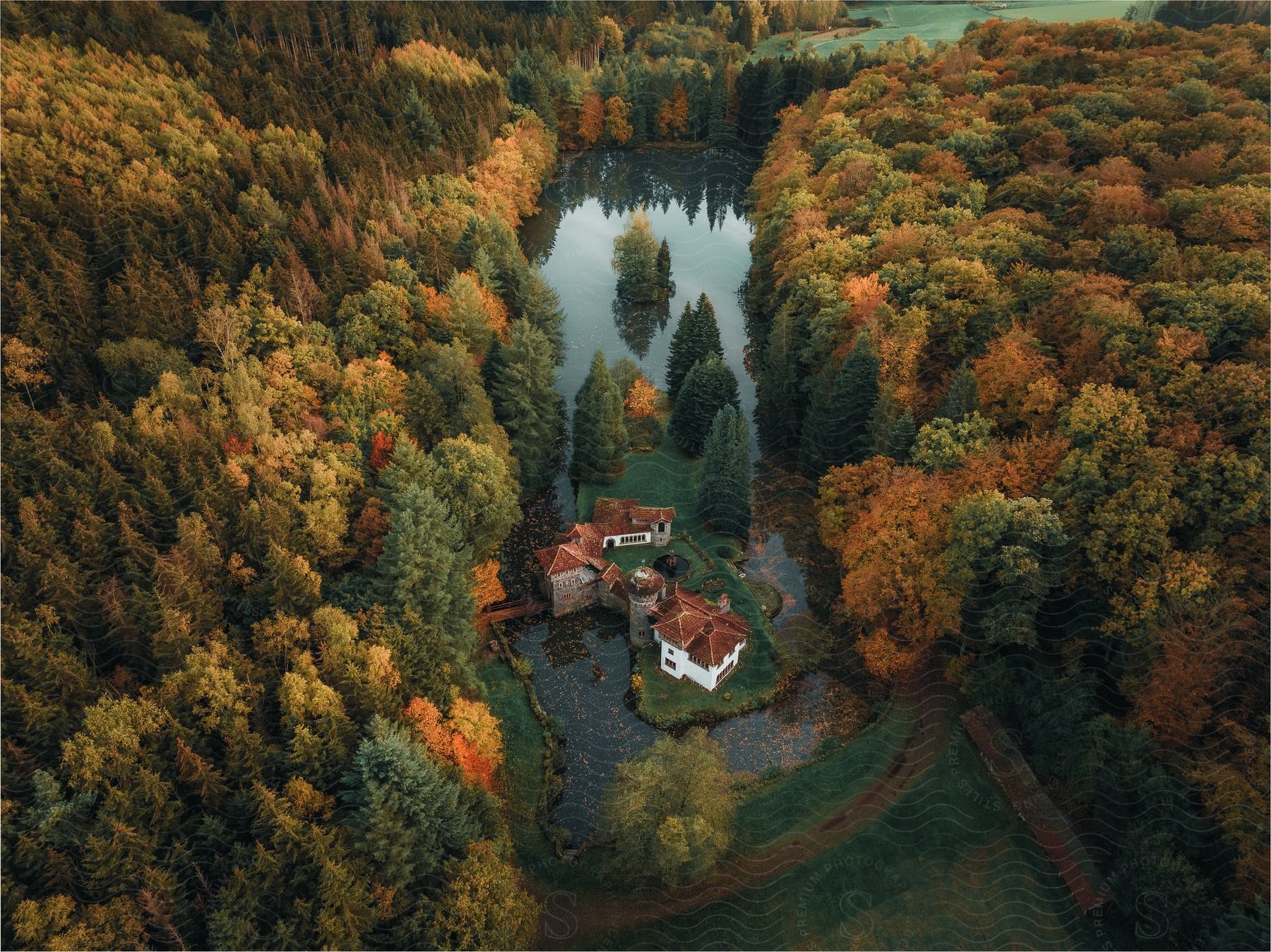 A white house, set in a serene, autumnal environment. The house is surrounded by dense, colorful forest, and a nearby lake reflects the surrounding trees.