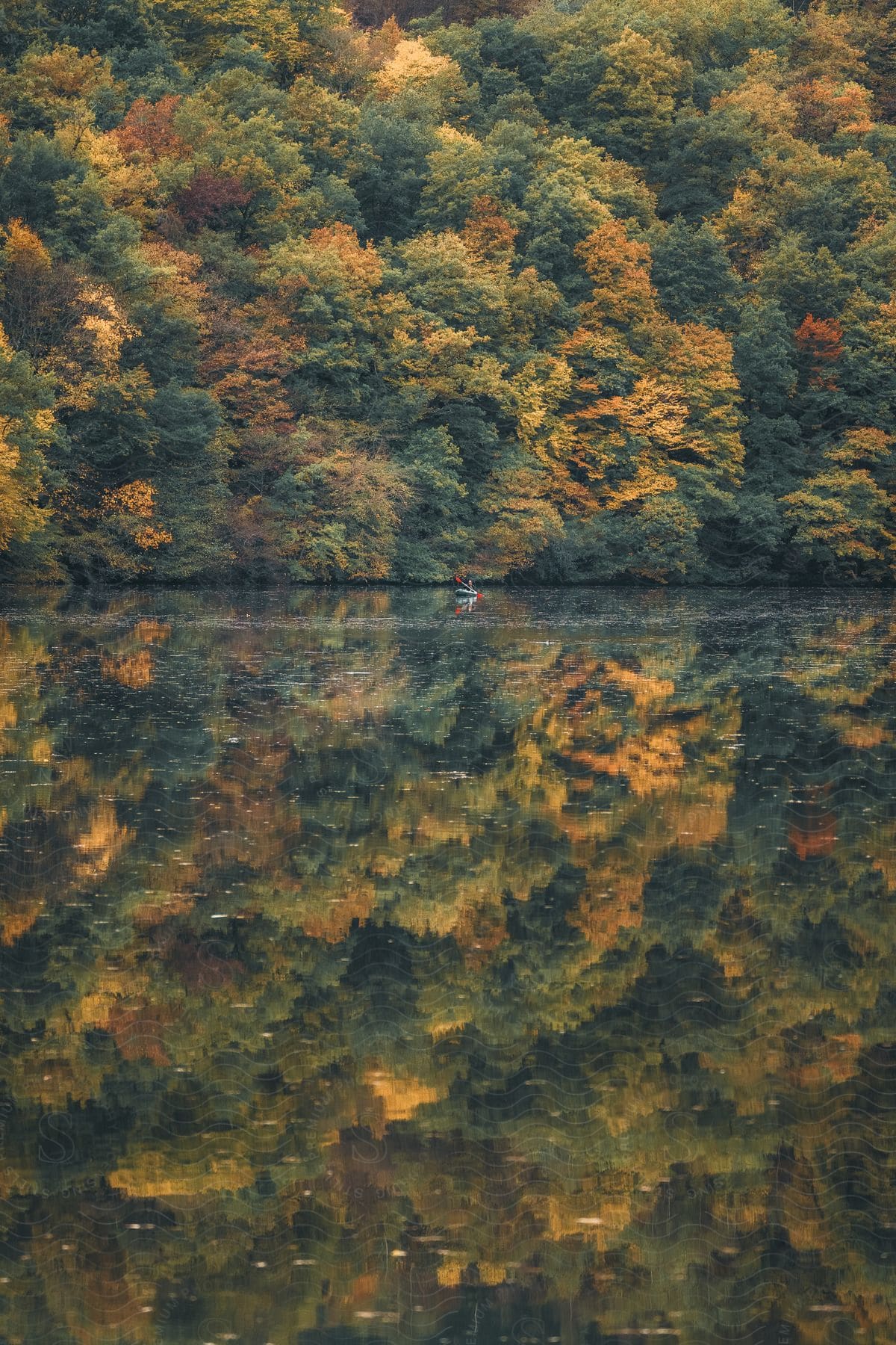 A person paddling a kayak on a tranquil lake, surrounded by autumn trees reflected in the water.