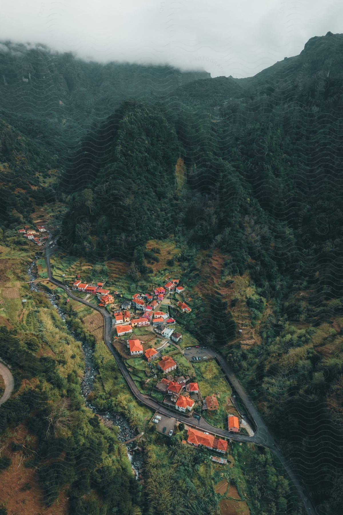 Village of houses with orange roofs sits in the valley of a large, tree-covered mountain.