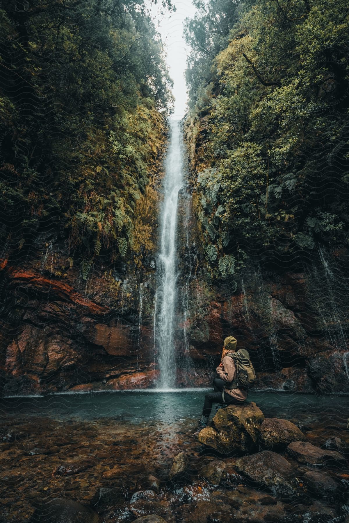 Woman sitting on a rock and facing a natural landscape of a waterfall in the forest