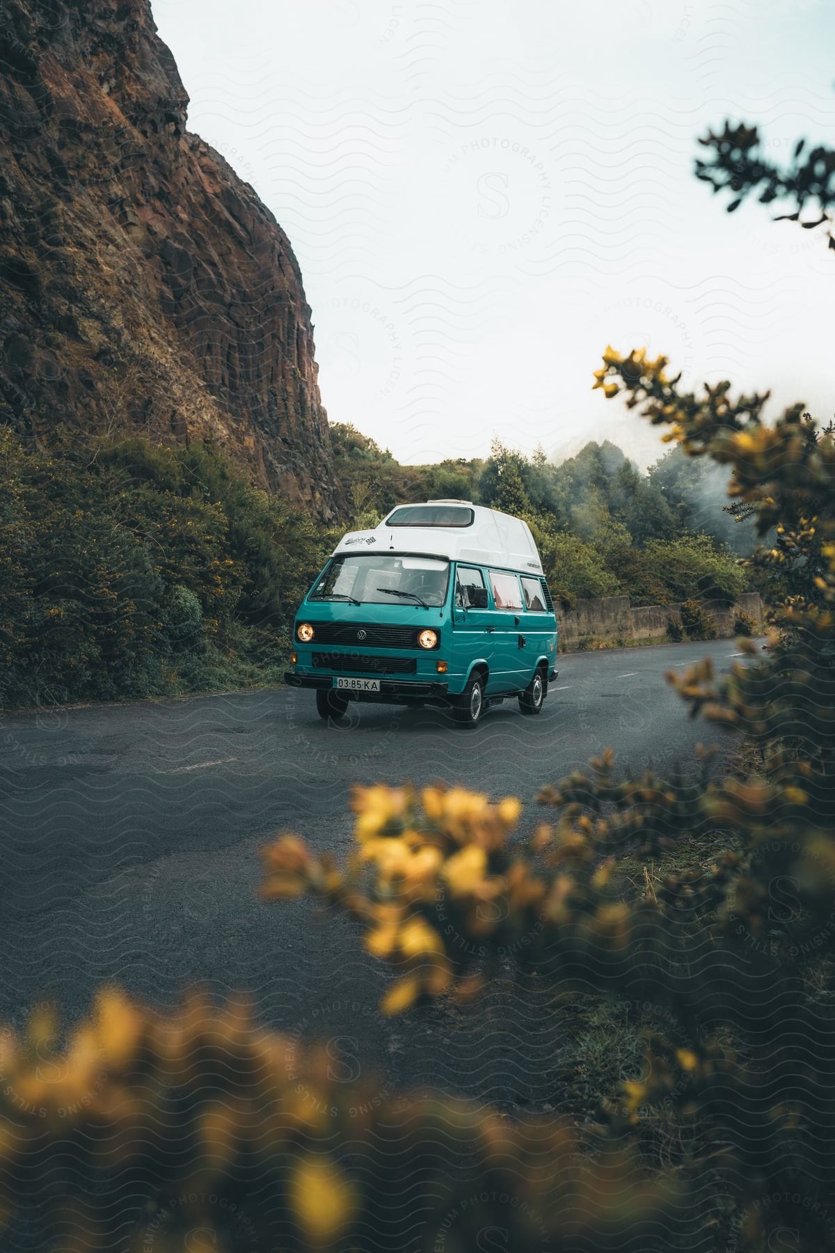 A blue Volkswagen Type 2 on an asphalt next to mountains in a natural environment.