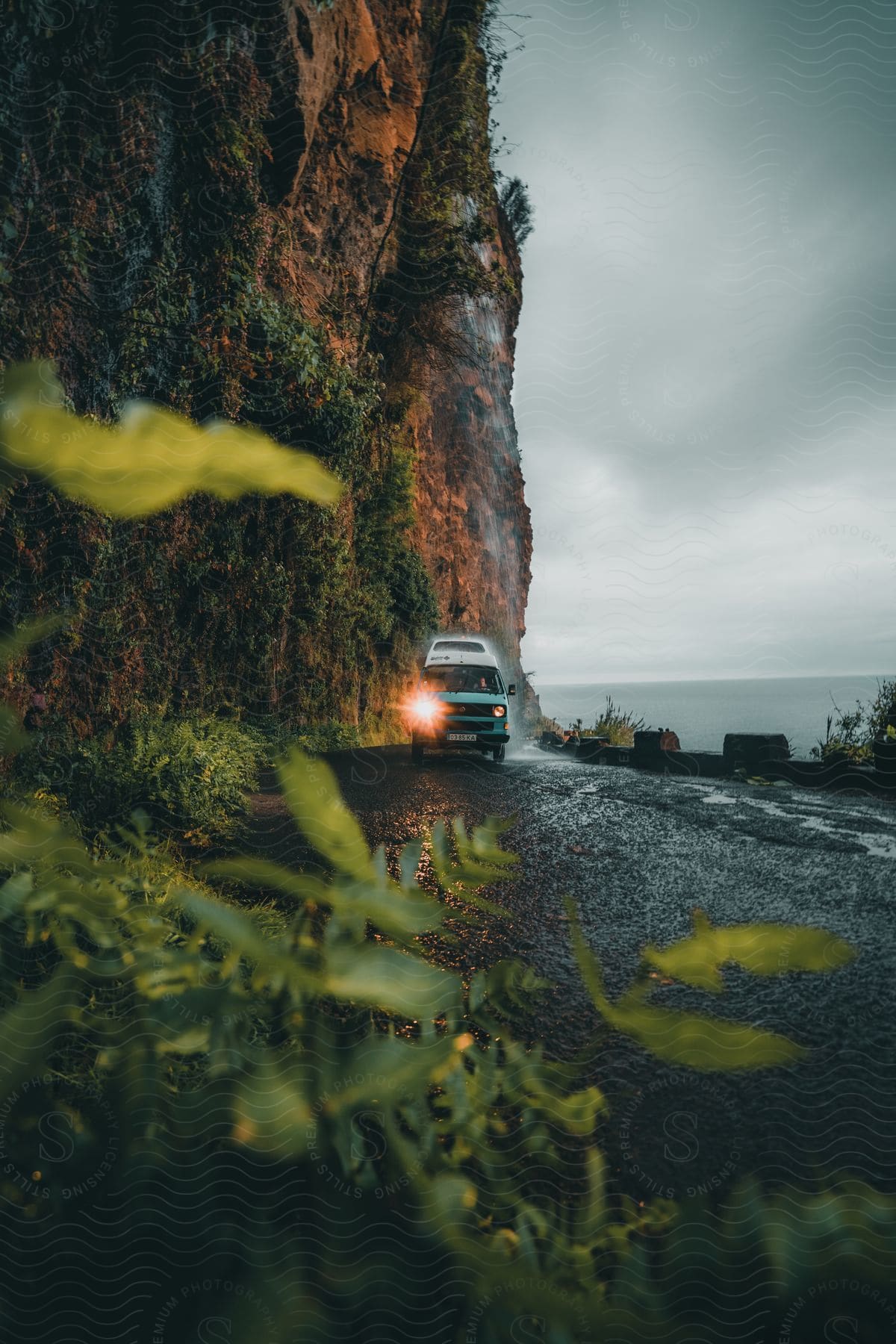 A van driving on a wet coastal road next to a large rock wall.