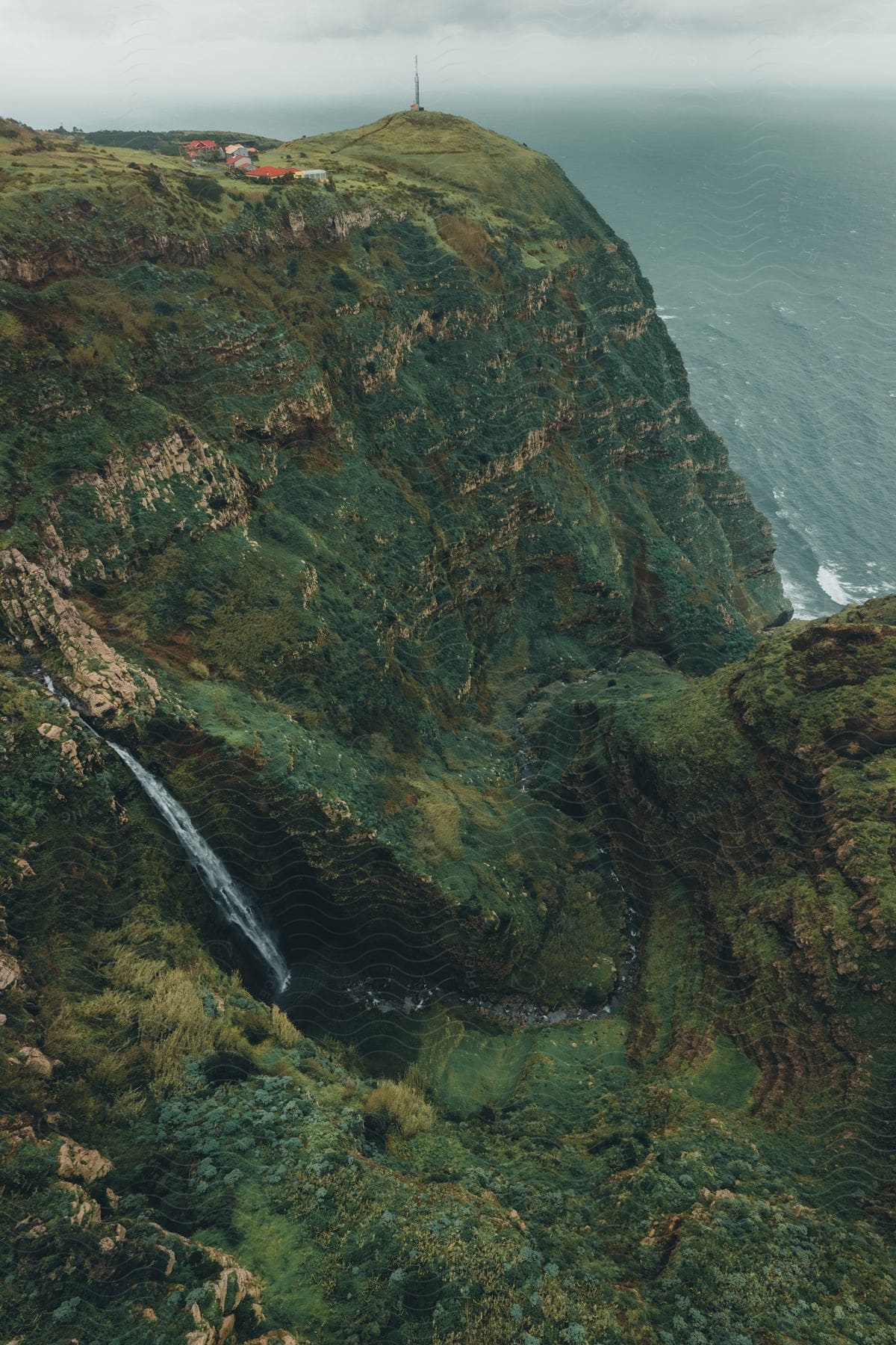 Atop the mountain, a small town gazes over the ocean below. A lighthouse stands beside the town's edge, illuminating the sea. Positioned high above the waves, the town commands a panoramic view of the ocean.