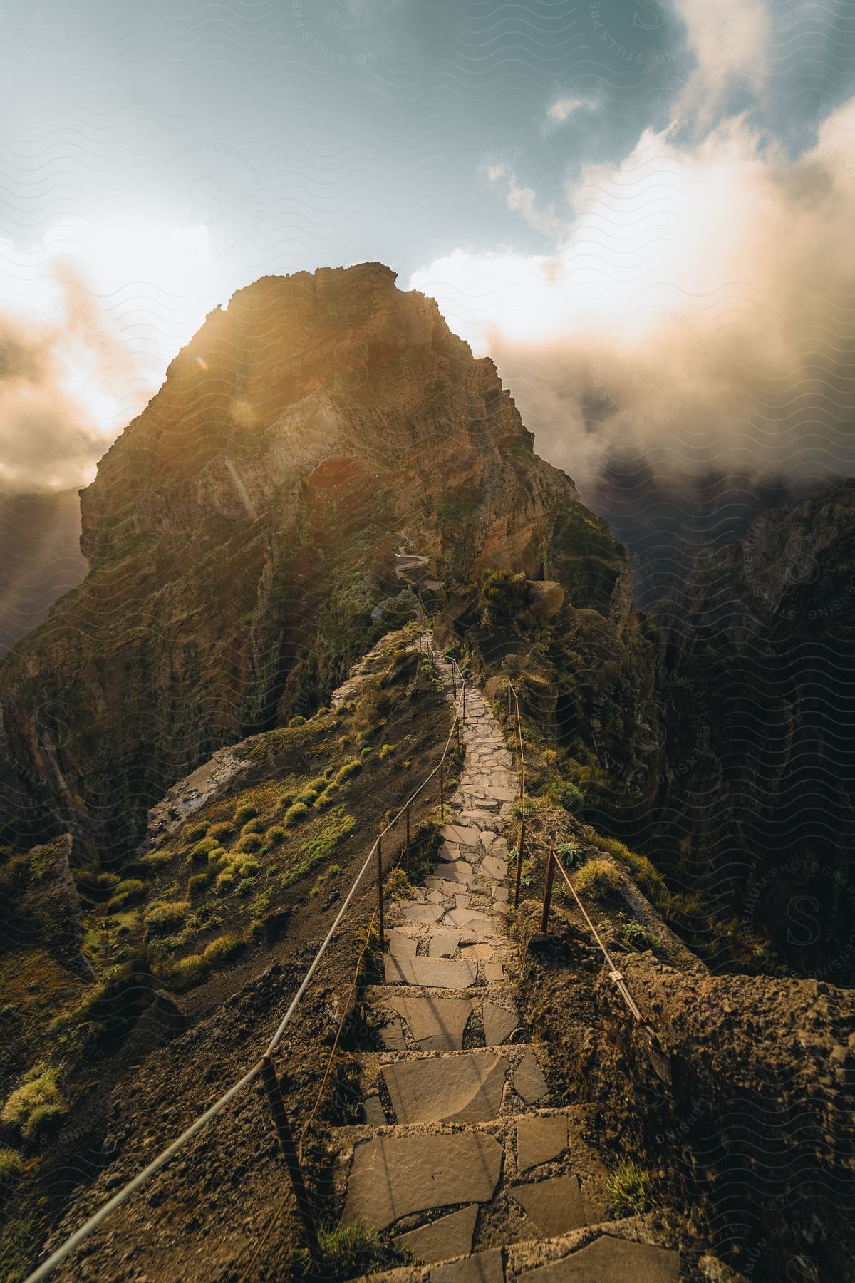 A steep stone-paved trail leads up to a cloud-covered peak bordered by a rope railing