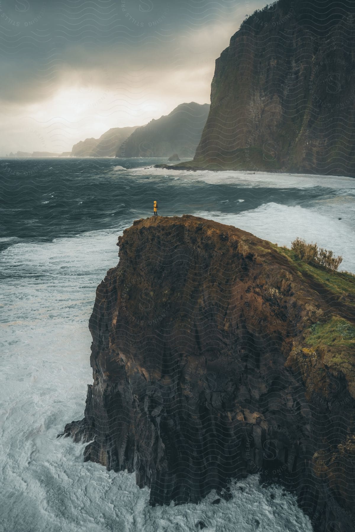 A person standing on the edge of a cliff over a turbulent sea.