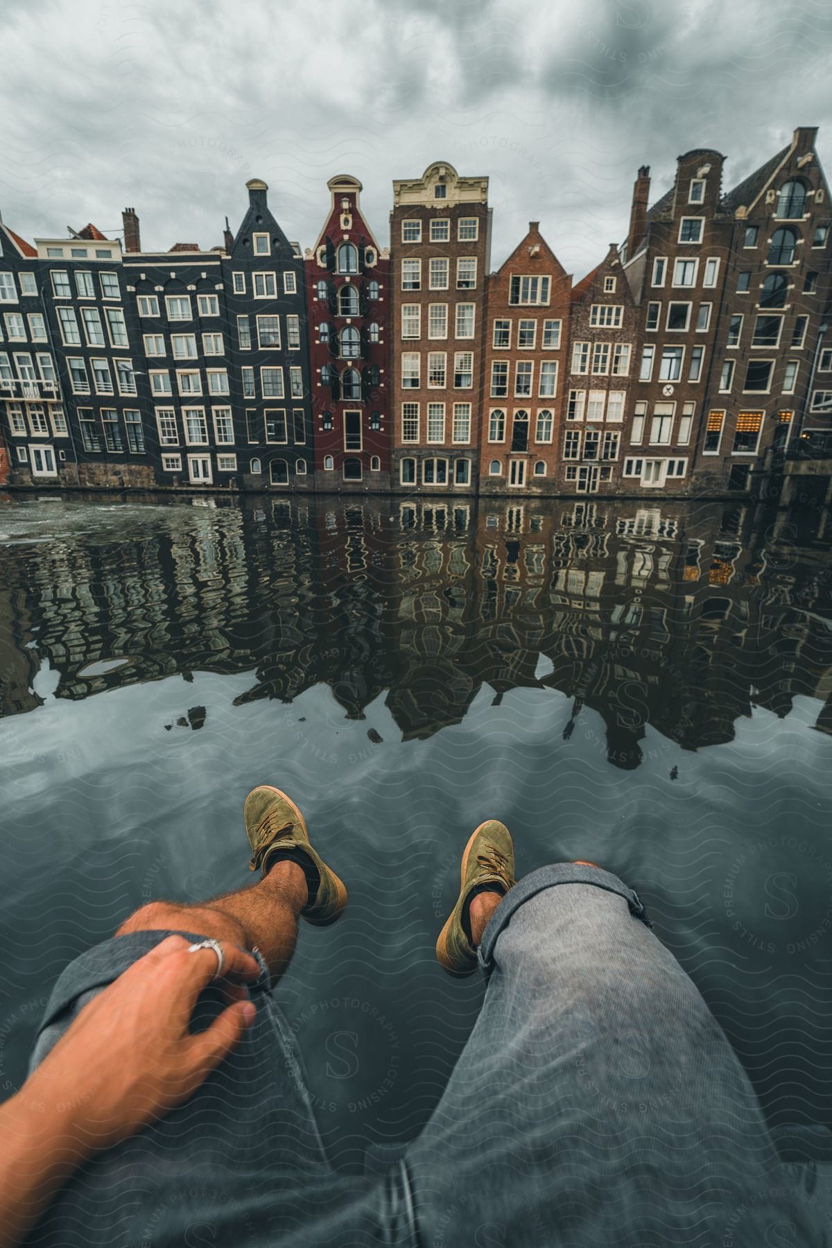 A man sitting along the water looking at buildings in a city.