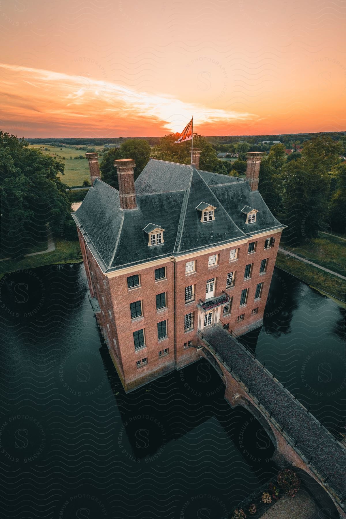 Mansion surrounded by a moat at sunset with rural backdrop.