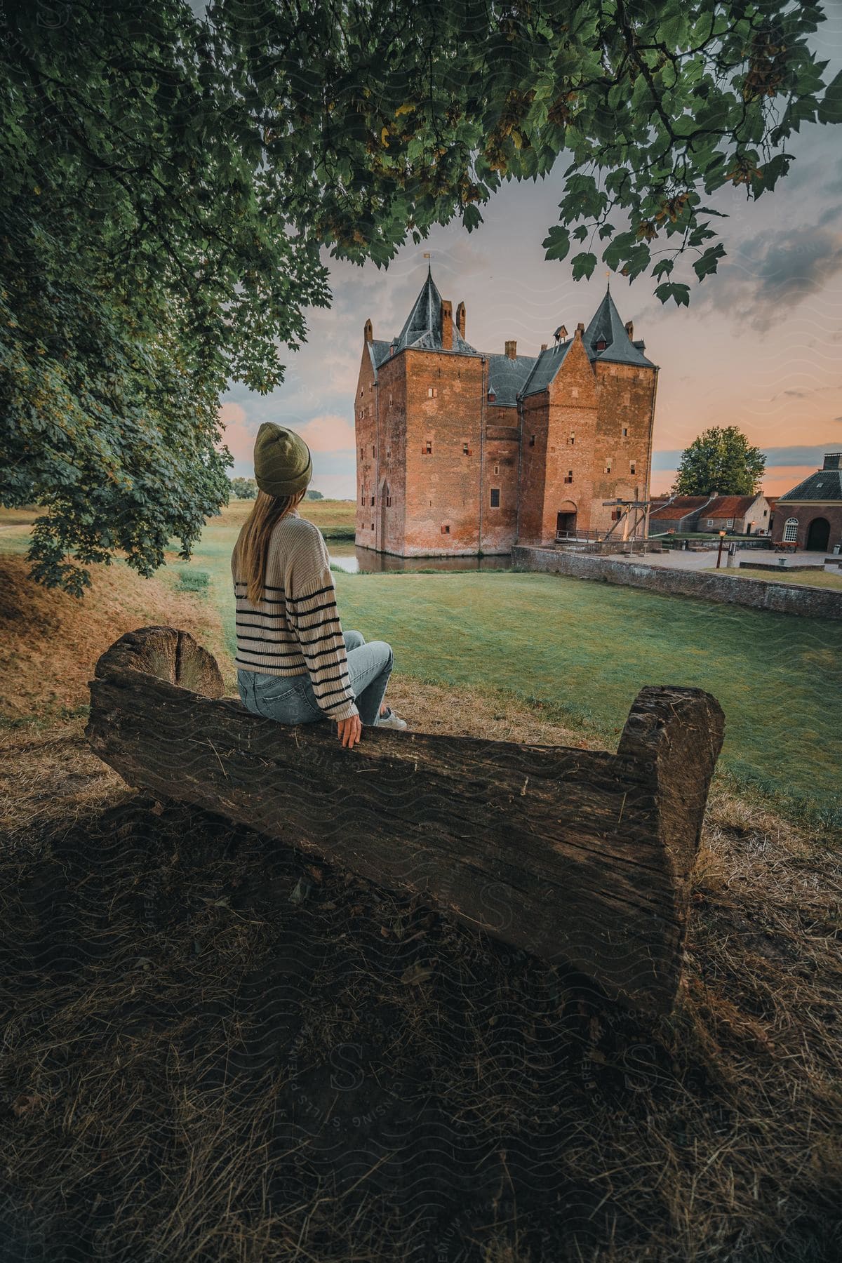 A person is sitting on a rustic wooden bench, contemplating a castle at dusk.