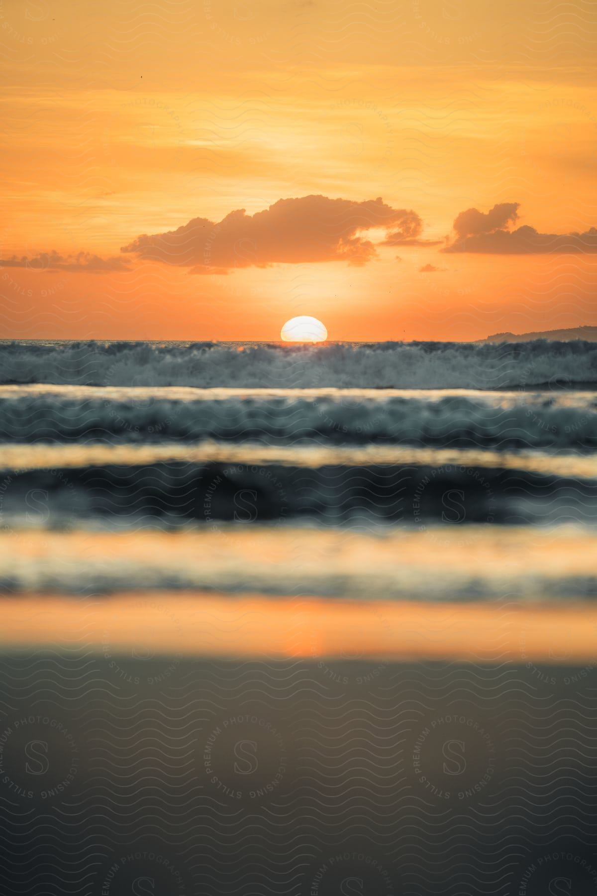 Sunset over the ocean with waves and the sun halfway below the horizon and clouds in the sky.