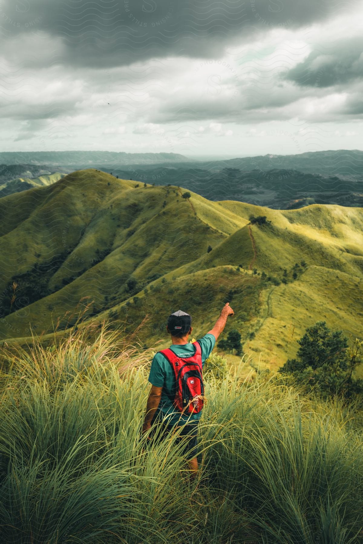 Man wearing a backpack stands on a hillside overlooking mountains