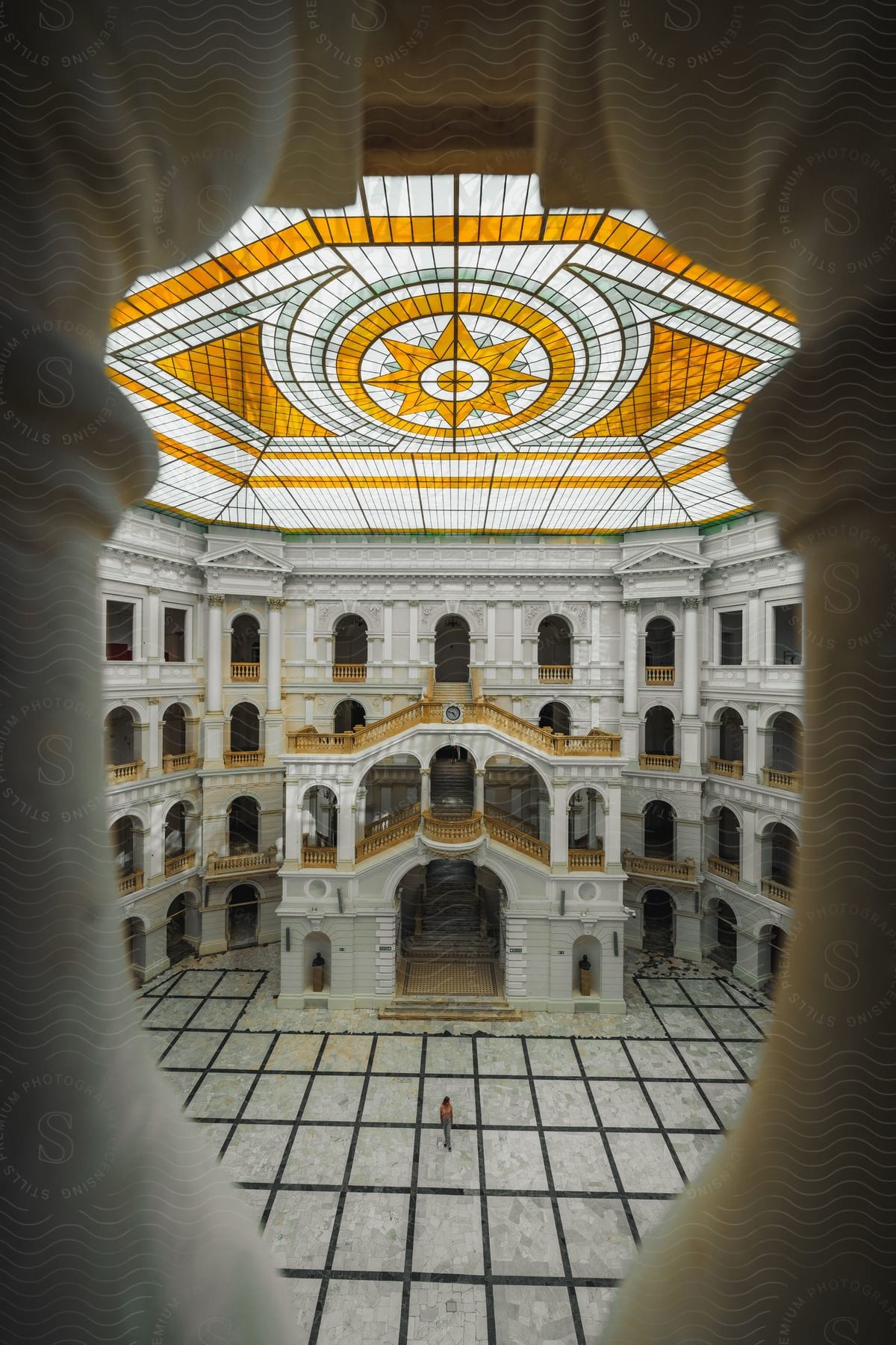 A covered patio where the ceiling has a yellow stained glass and many windows, stairs and corridors