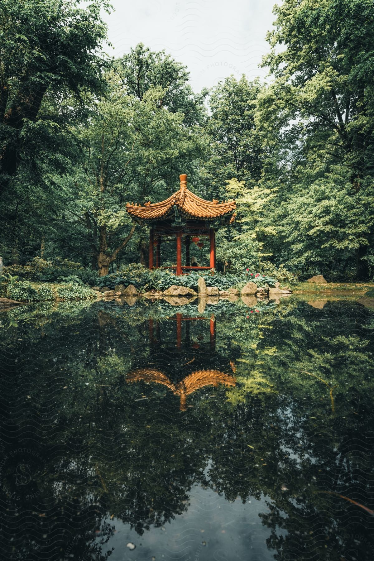 s a small, octagonal building with a red roof in the middle of a pond