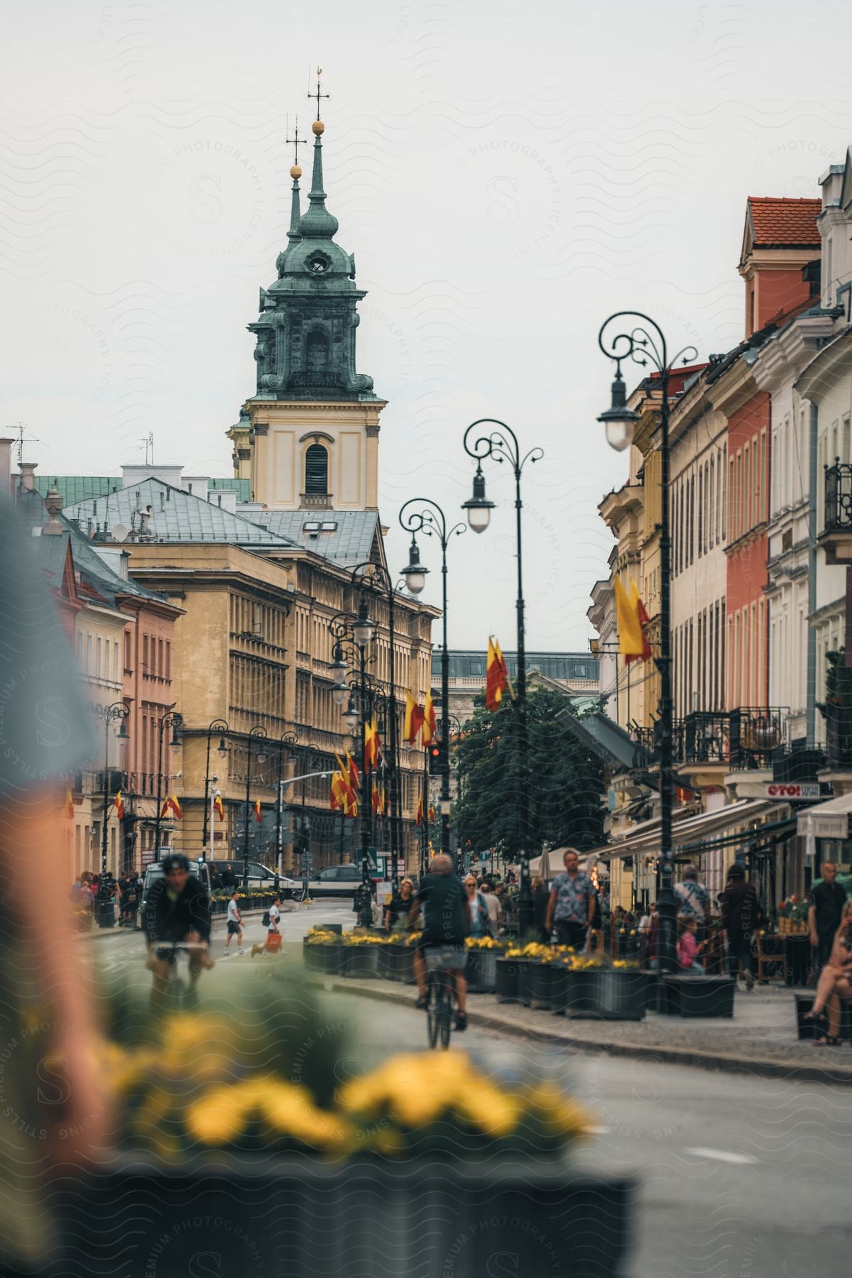 A busy street with bicyclist and pedestrians is lined by buildings with picturesque architecture.