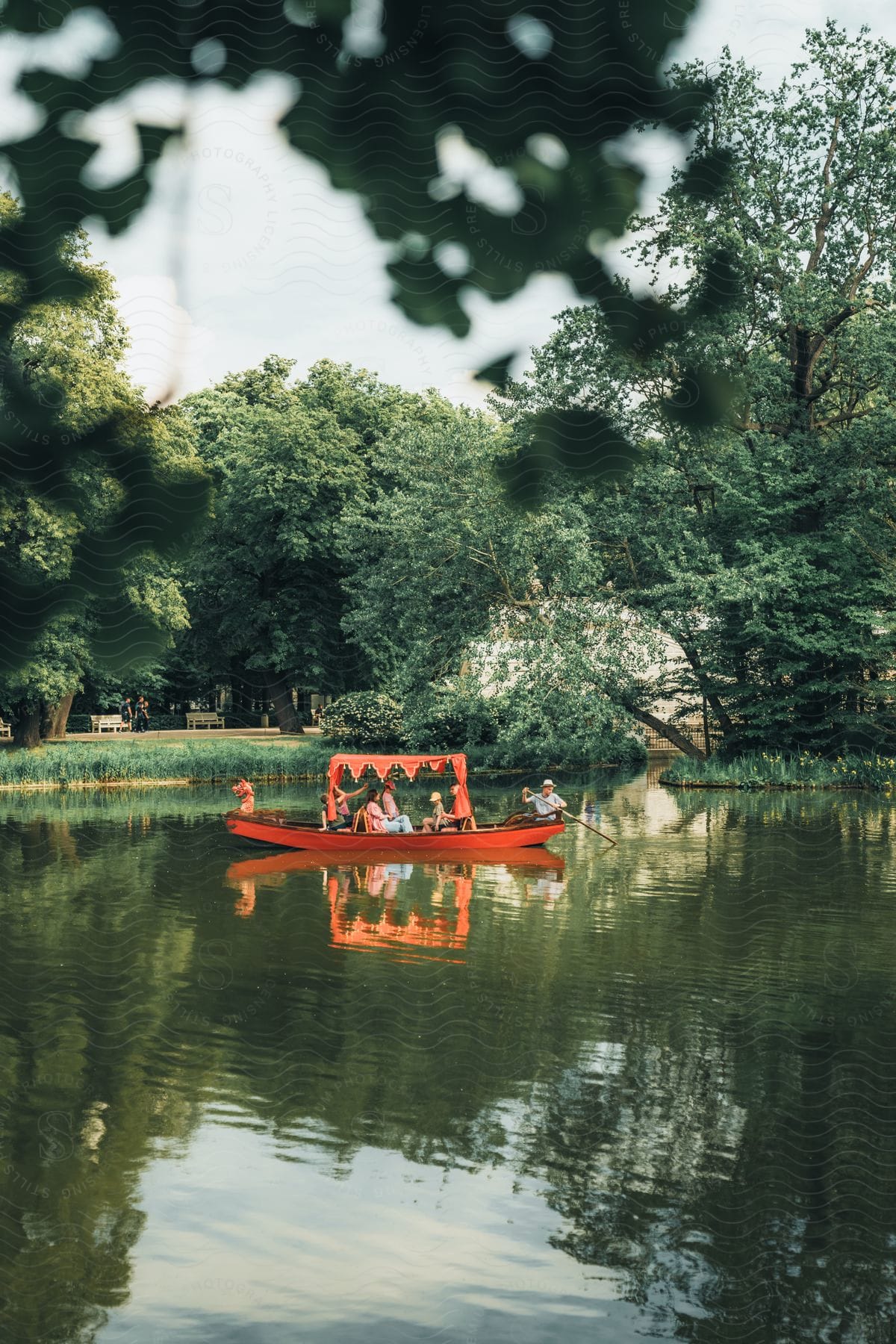 Lake with a reddish wooden boat with people touristing on a blue sky day with clouds