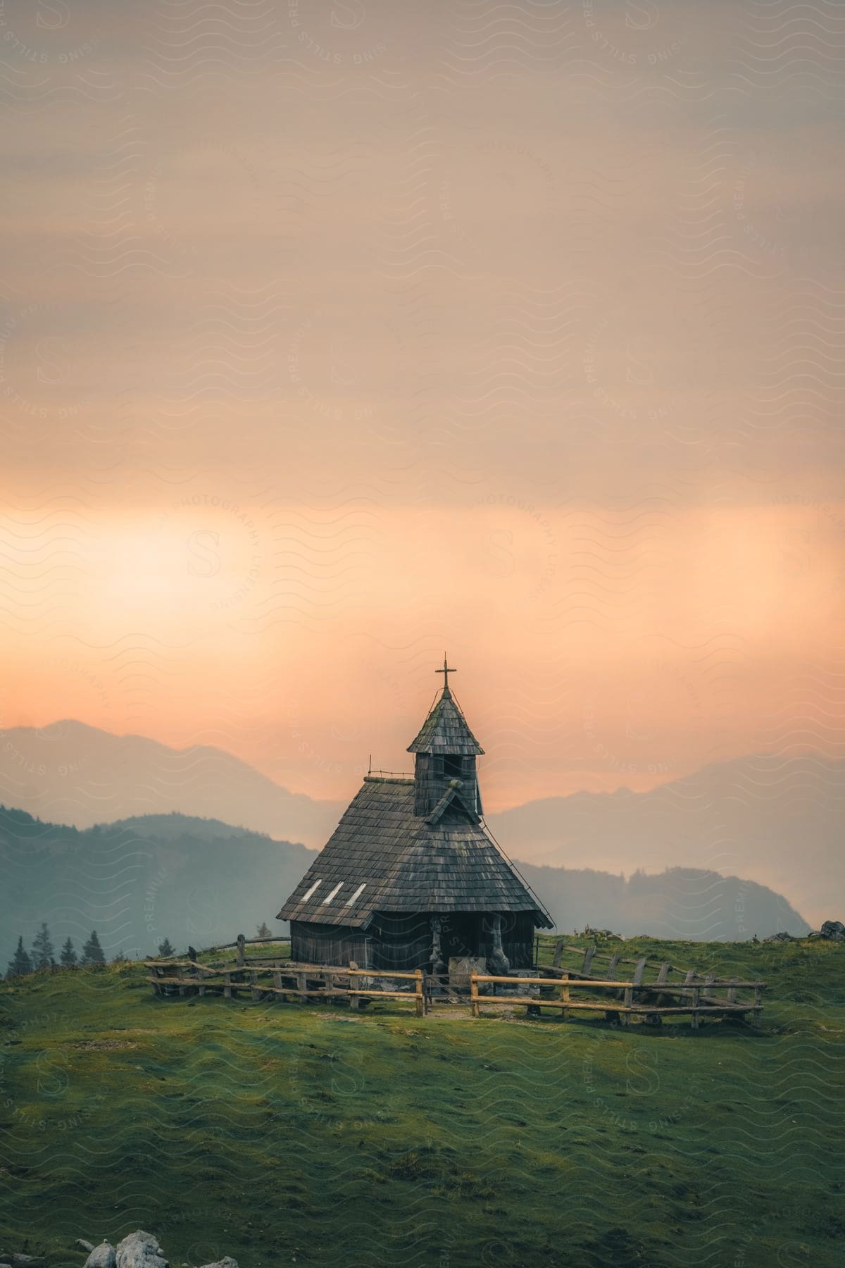 A rural church on a grass covered mountain with mountains in the distance under a foggy sky