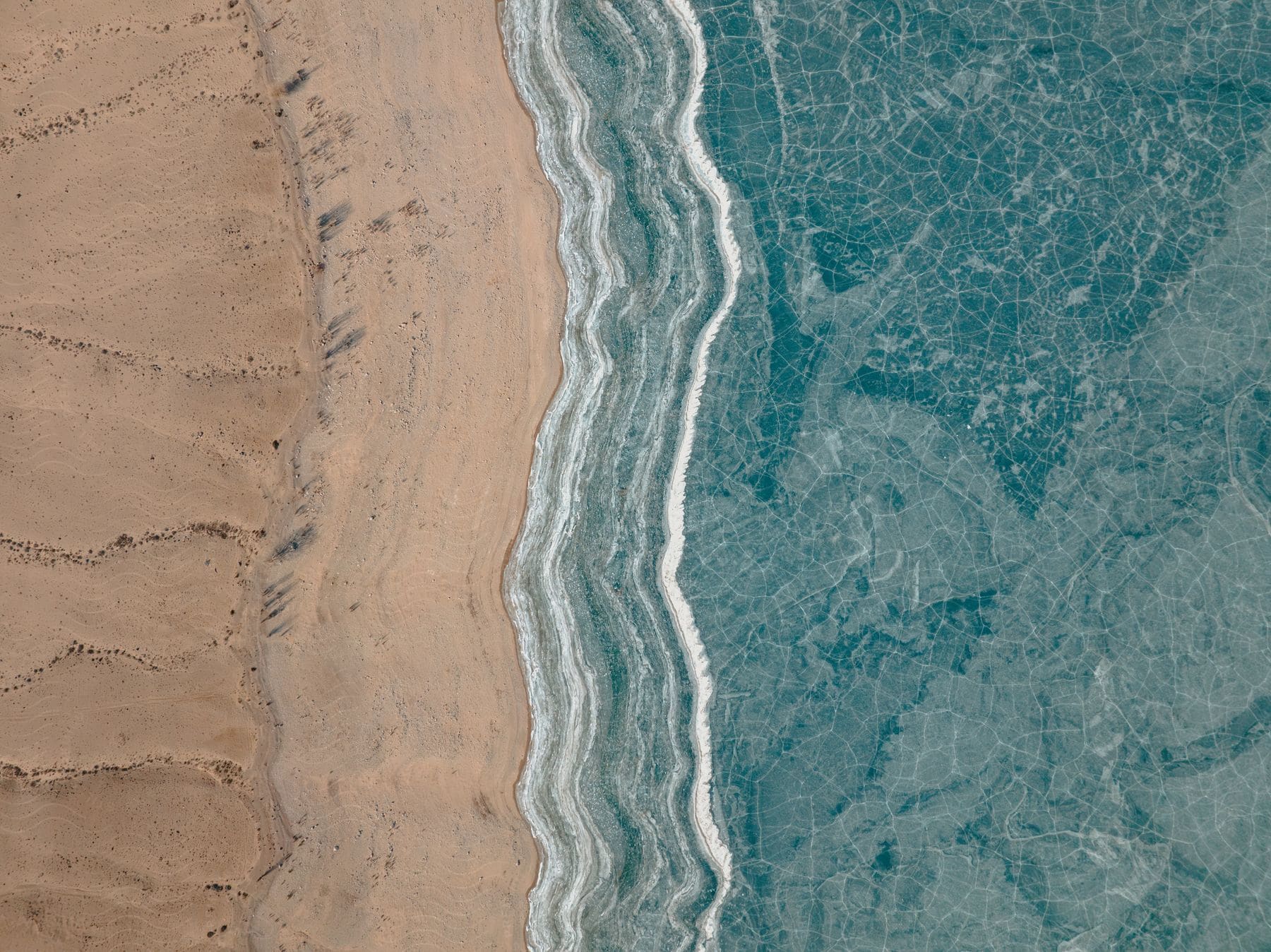 Top view of a turquoise sea lined with beach sand