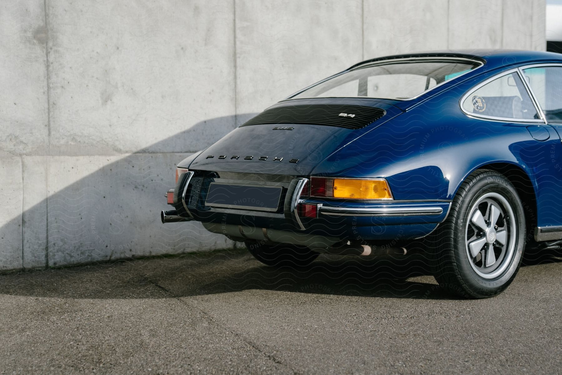 Rear Of A Blue Porsche 911 Next To A Gray Wall