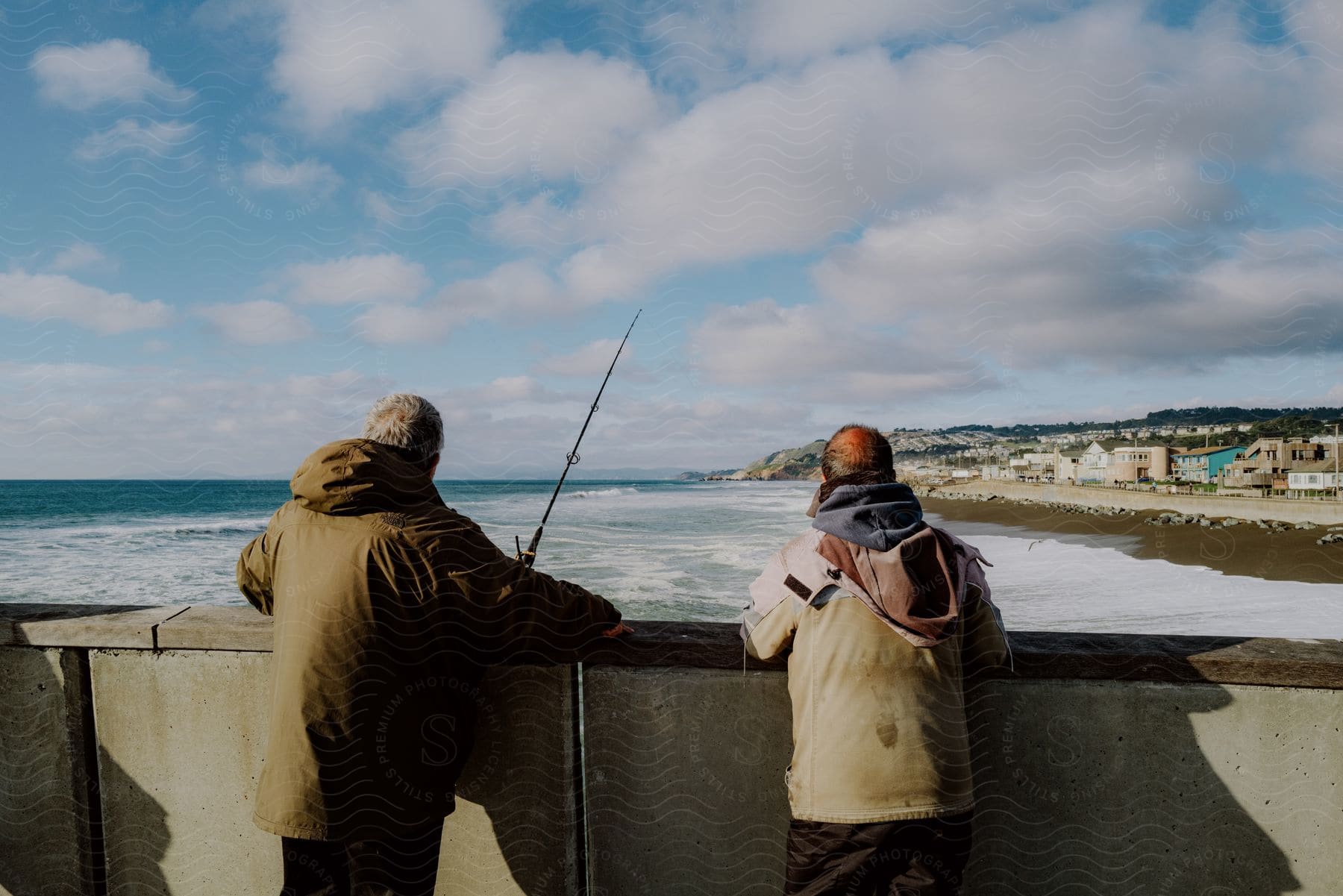 Two people with their backs turned, standing by the sea. They seem to be fishing or simply enjoying the coastal scenery.