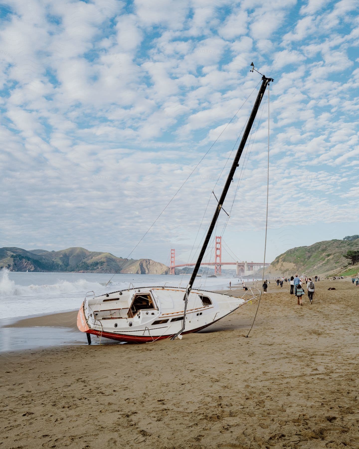 A beached sailboat with a tilted mast on a sandy beach with the Golden Gate Bridge in the background.