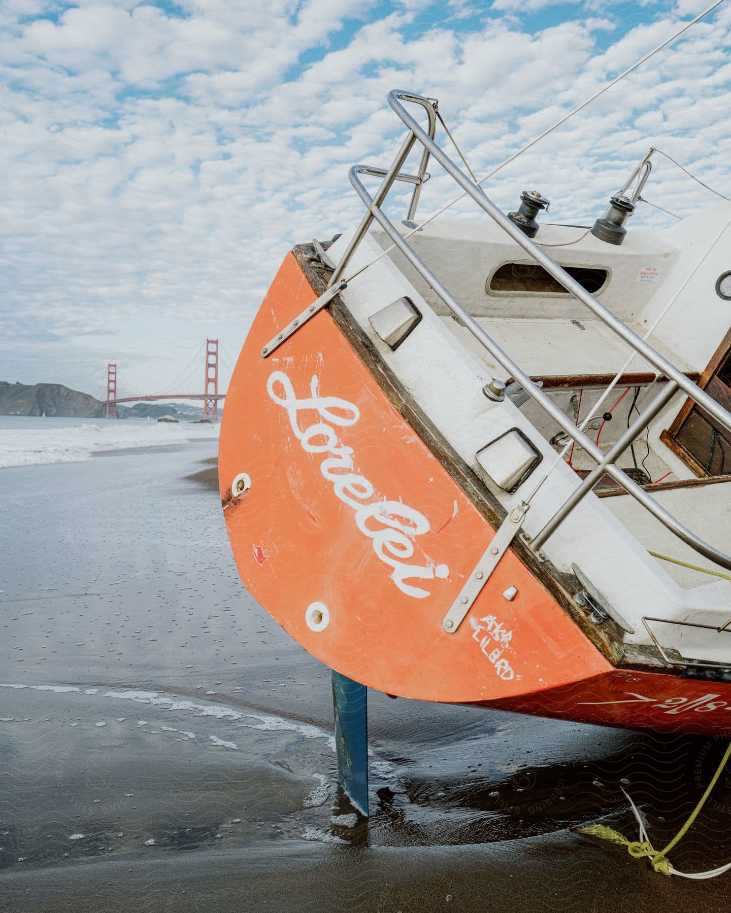 Boat leans on support on the beach with the Golden Gate Bridge in the background on a cloudy day.