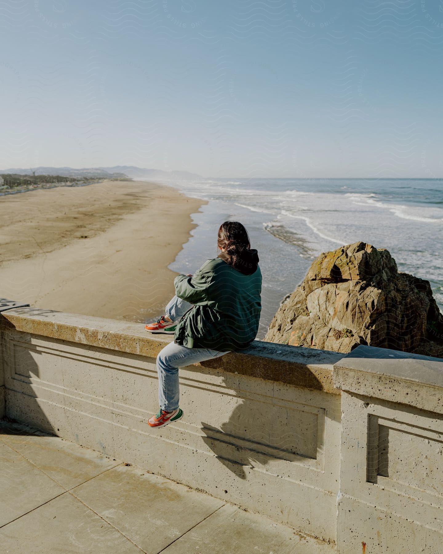 A woman looking over the beach on a winter day wearing a jacket.