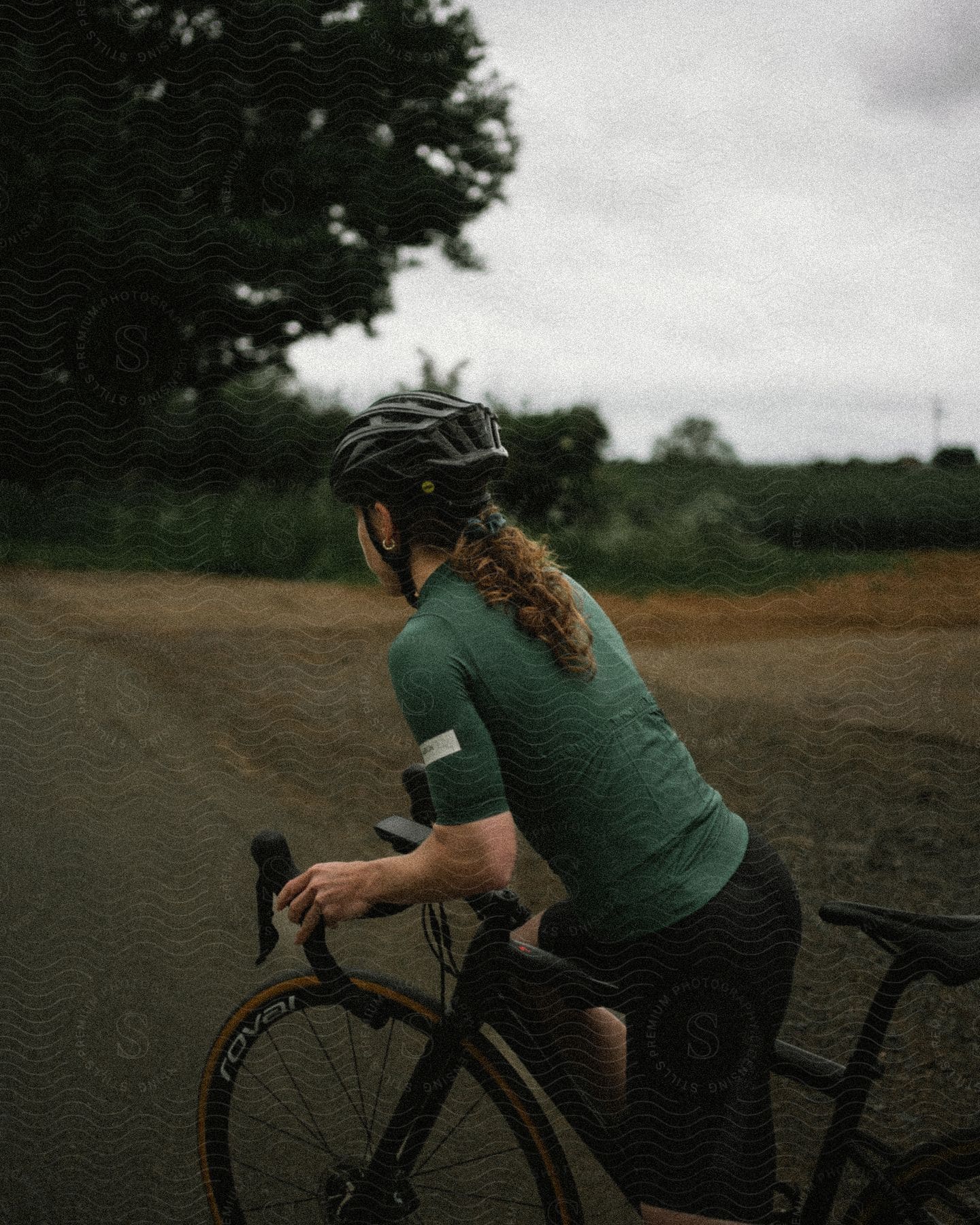 A cyclist begins riding her bike on a cloudy, summer day.