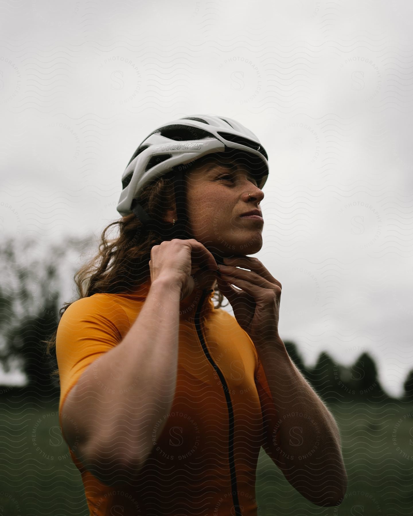 Woman tying her cycling helmet accessory while standing in an open field