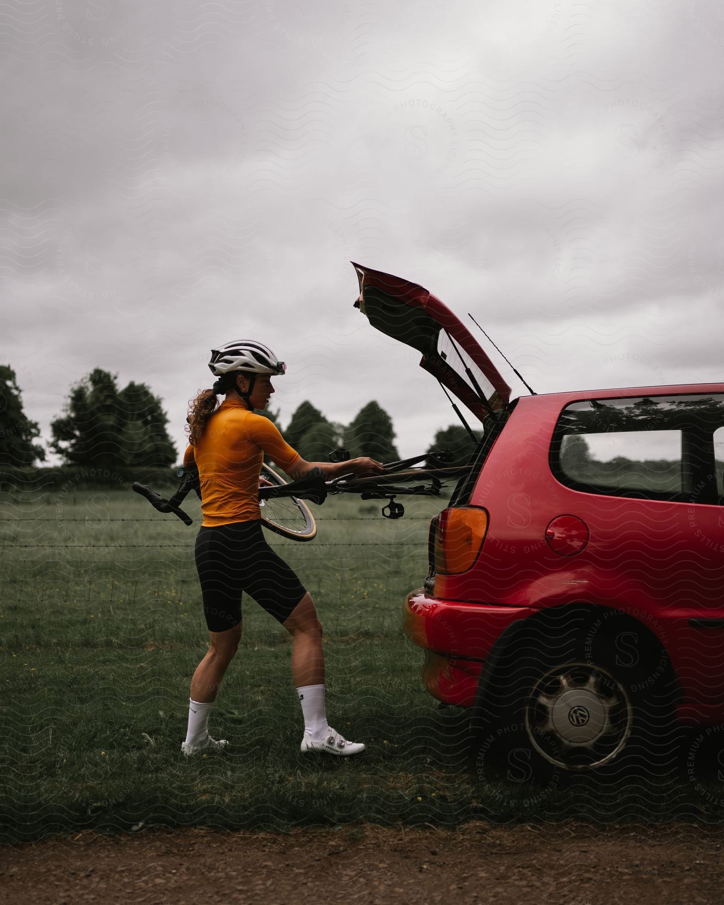 a female cyclist taking her bike off the trunk of a car on a cloudy day