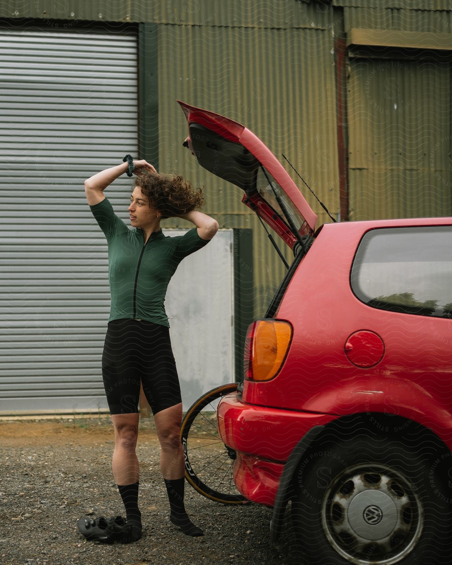 Young woman next to her car with open trunk fixing her hair while wearing a cycling outfit