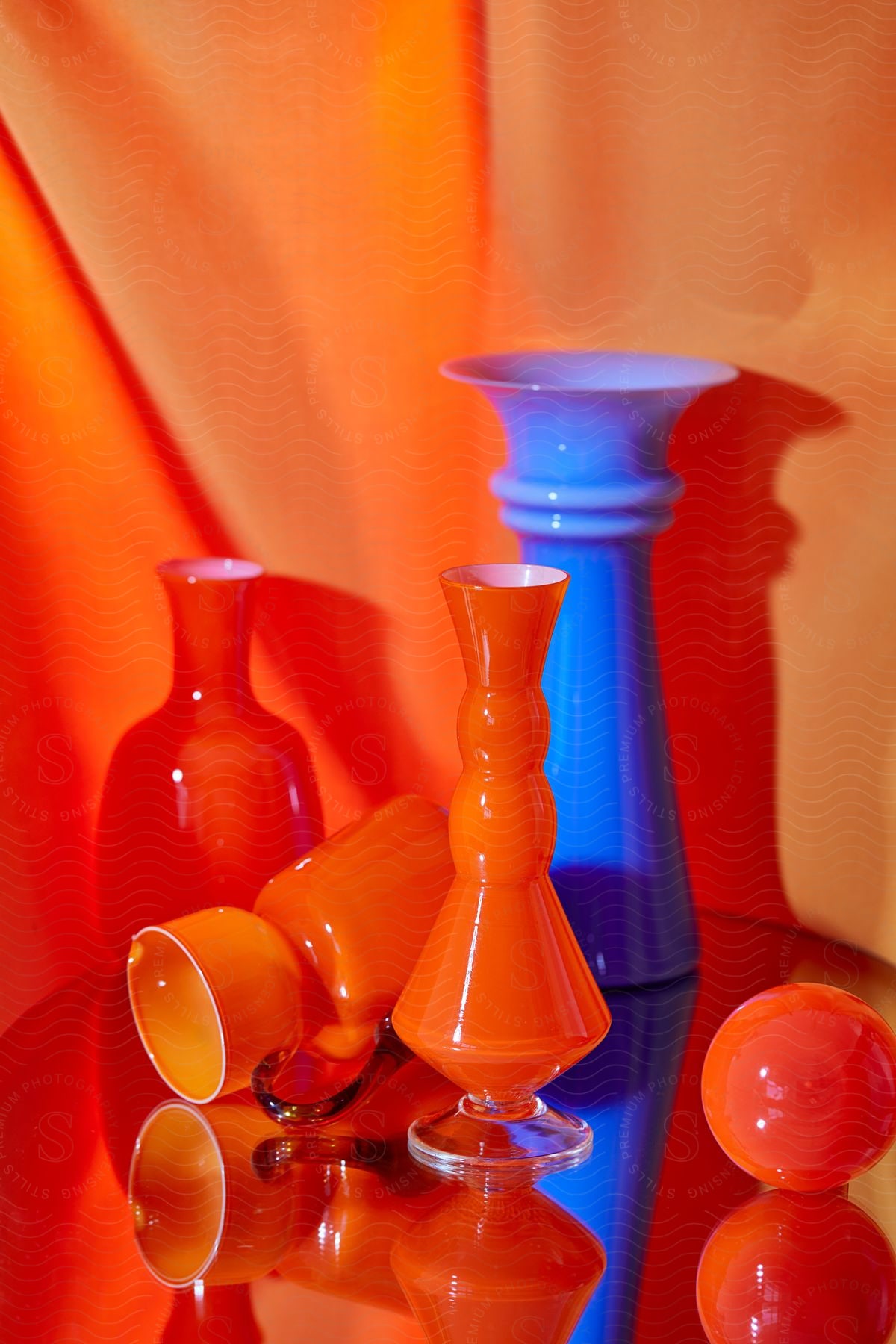 Glossy surface reflects bright vases sitting next to orange curtain.