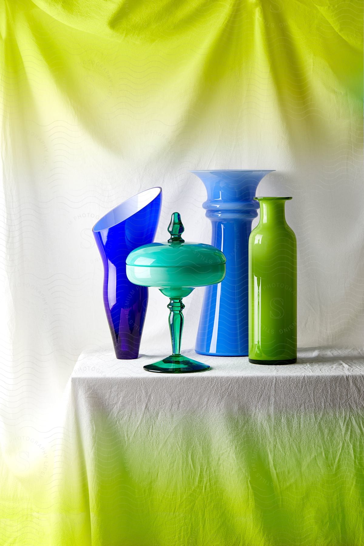 Vibrant glassware in cool tones contrast against a sunny lime backdrop.