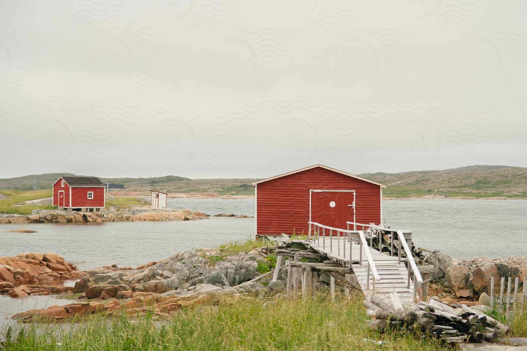 A red house with a wooden bridge and behind it there is a huge lake and on the other bank there is another red house