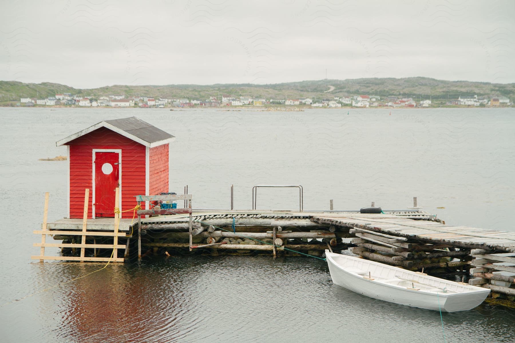 Small boat docked at a pier with a small red building overlooking a coastal community