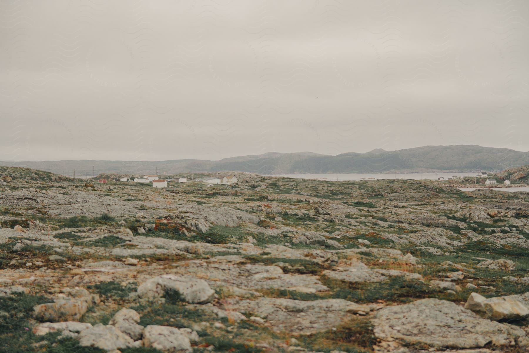 Buildings along the coast with mountains across the water under a foggy sky