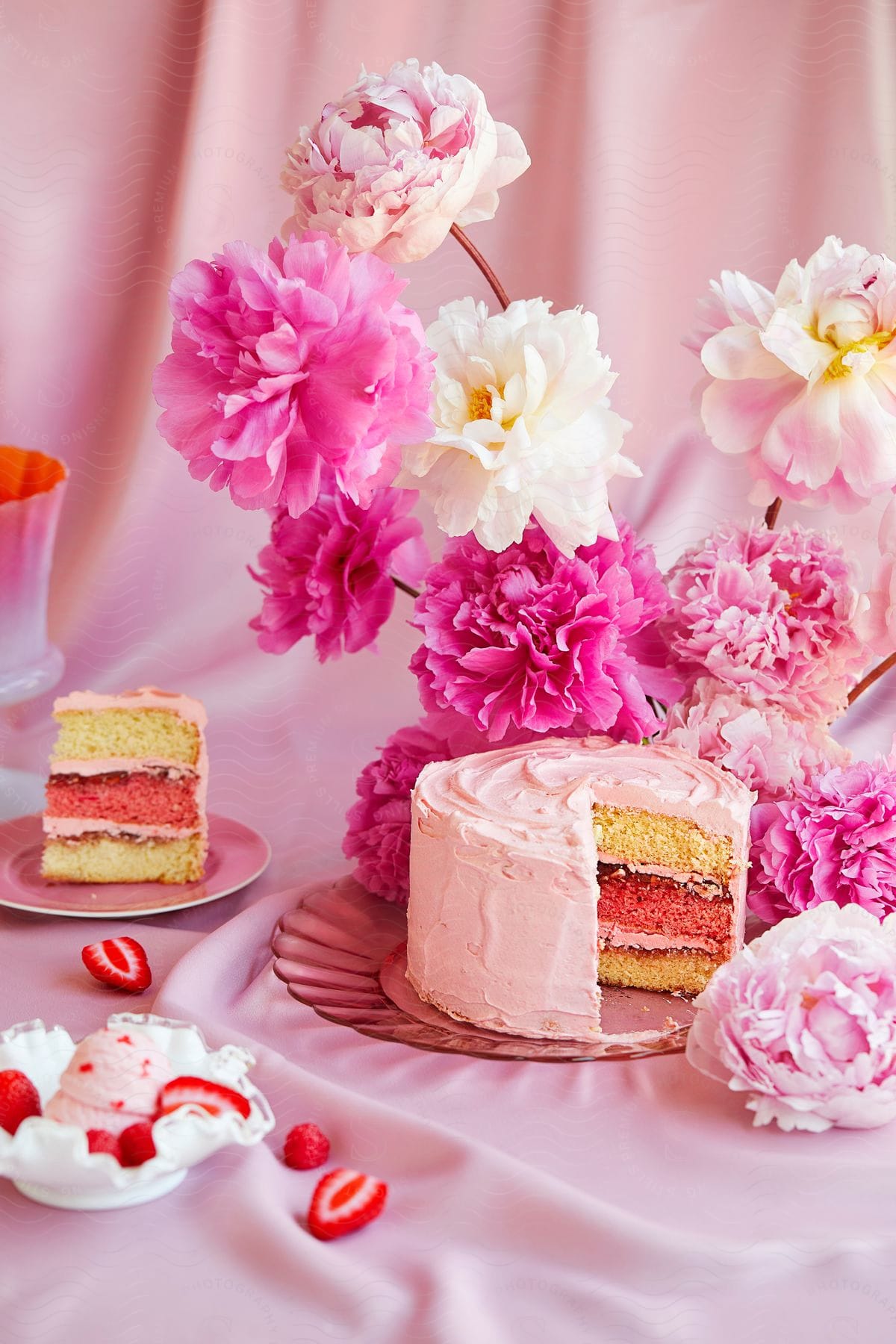 A pink party table with cake, ice cream, and flowers against a pink background.